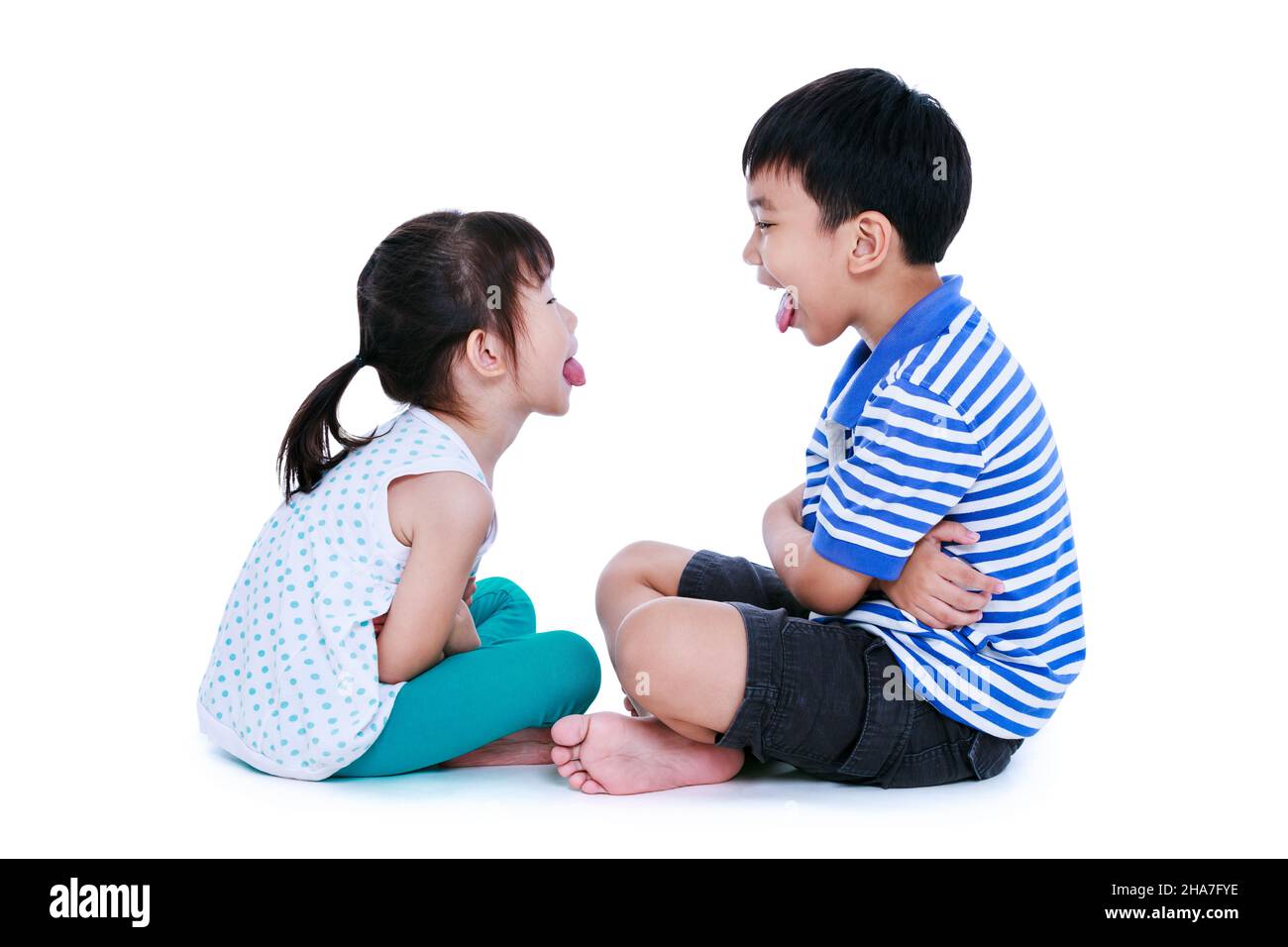 Bad behavior. full body of asian children sticking out tongues and mocking each other. Sister and brother sitting at studio, isolated on white backgro Stock Photo