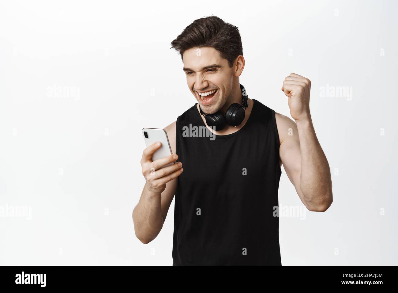 Happy guy with headphones, looking at phone and rejoicing, triumphing ...