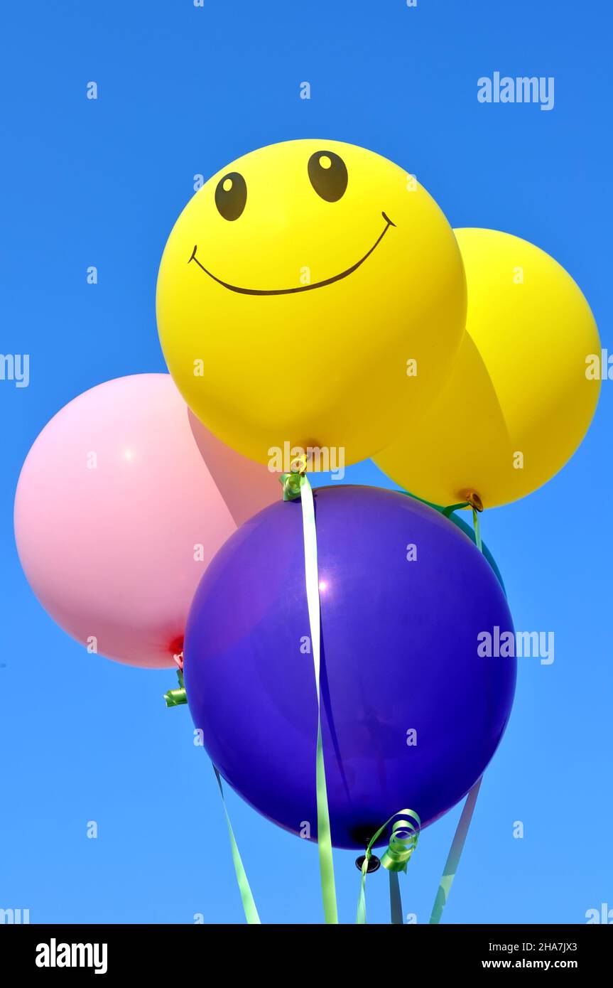 smiling balloon among of bunch of multicolored balloons in the city festival on clear blue sky background, vertical composition Stock Photo