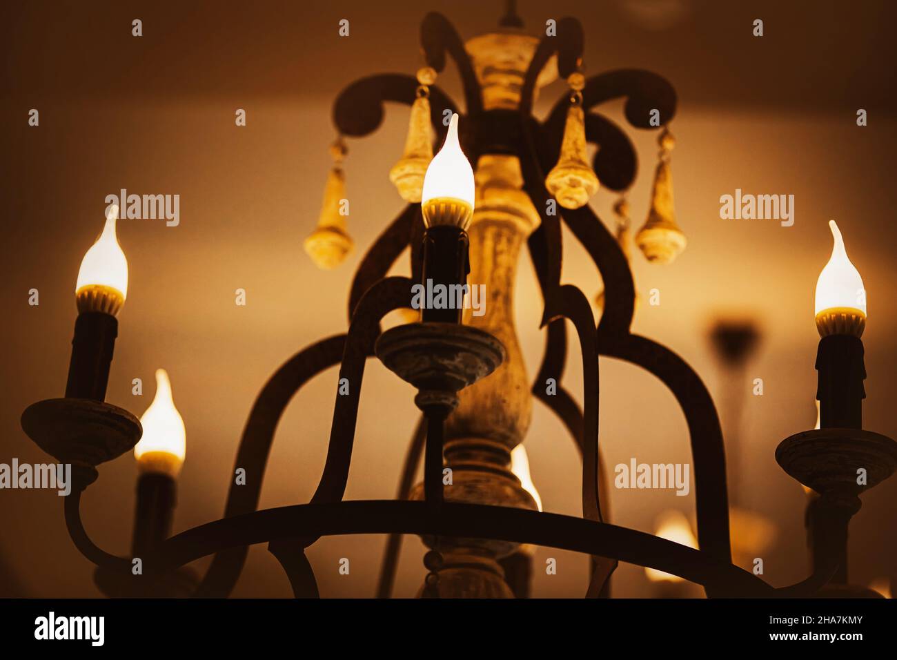 On an old elegant beautiful chandelier, lamps in the form of candles emit a bright cozy light in