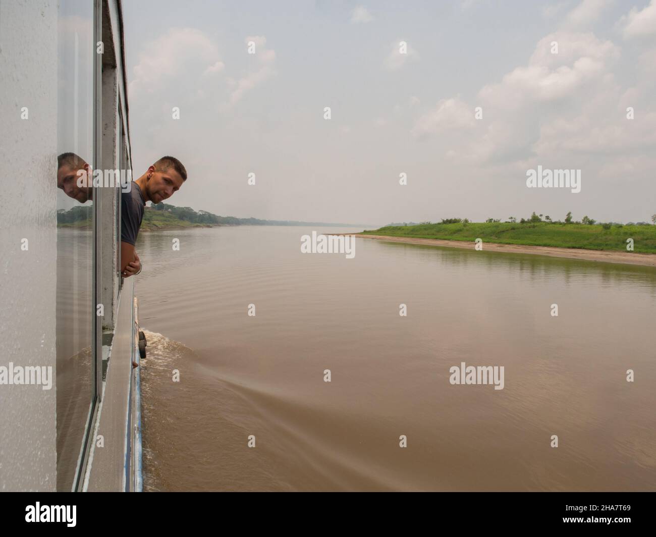 Amazon river, Peru - Sep, 2017: Caucasian globetrotter is looking through the ship window while is swimming via Amazon rainforest. Amazonia. South Ame Stock Photo