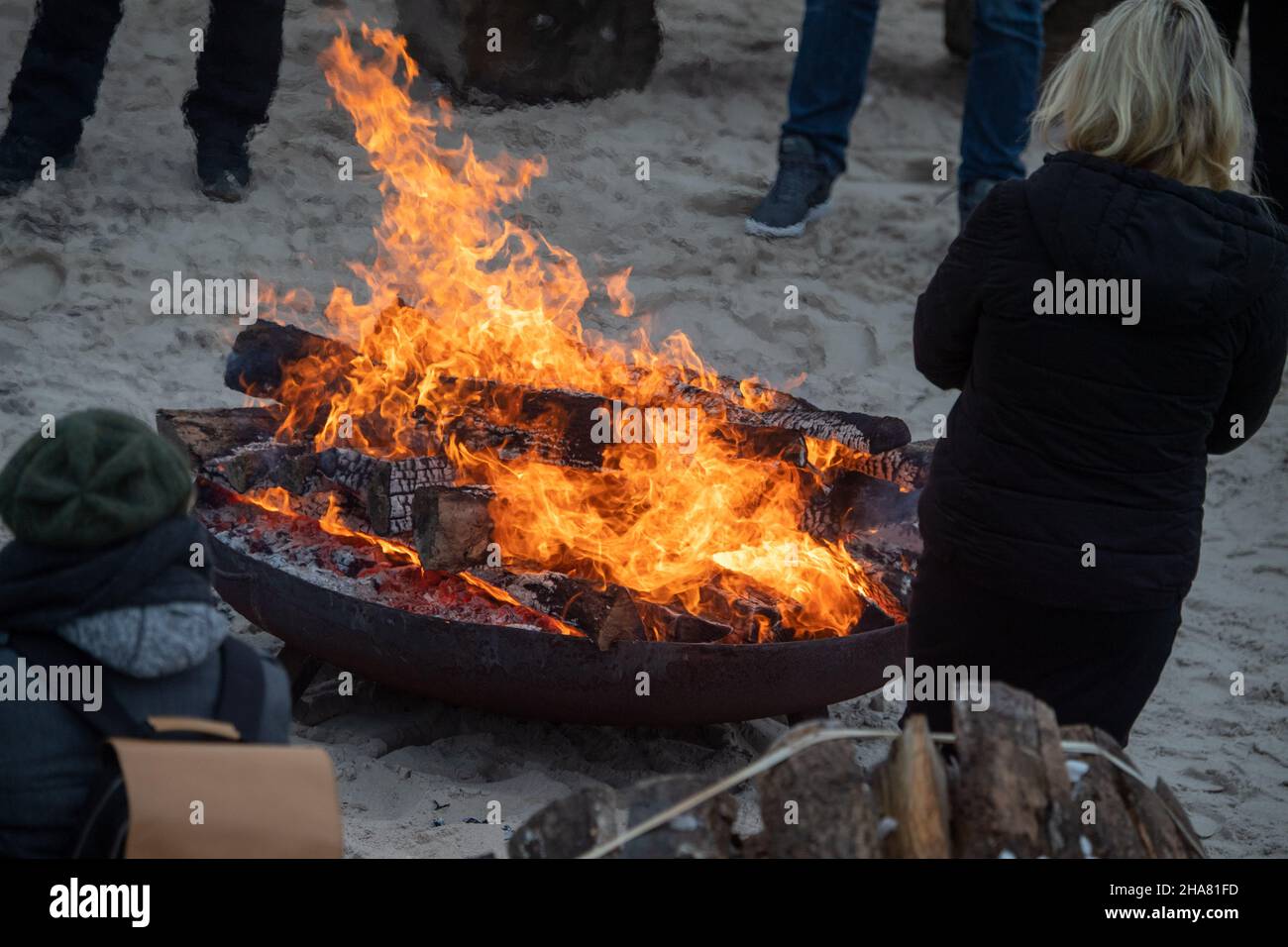 Binz, Germany. 11th Dec, 2021. A fire blazes in a fire bowl on the  snow-covered Baltic Sea beach on Usedom. In the foreground, the lettering  of a mulled wine tavern can be