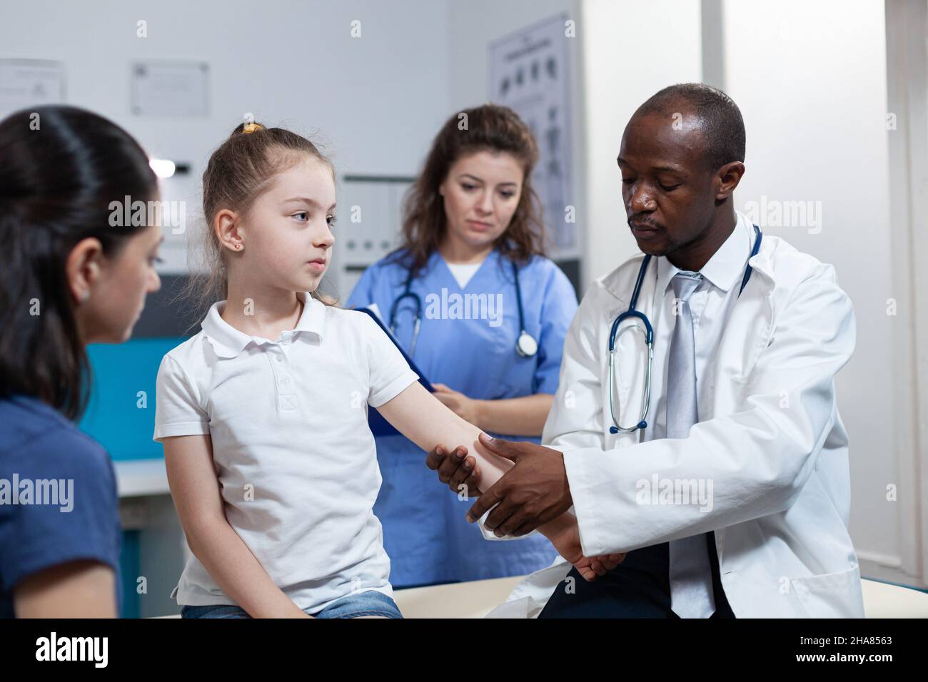 African american pediatrician doctor bandage fractured bone of girl patient during clinical physiotherapy in hospital office. Young child having broken arm after accident. Health care service Stock Photo