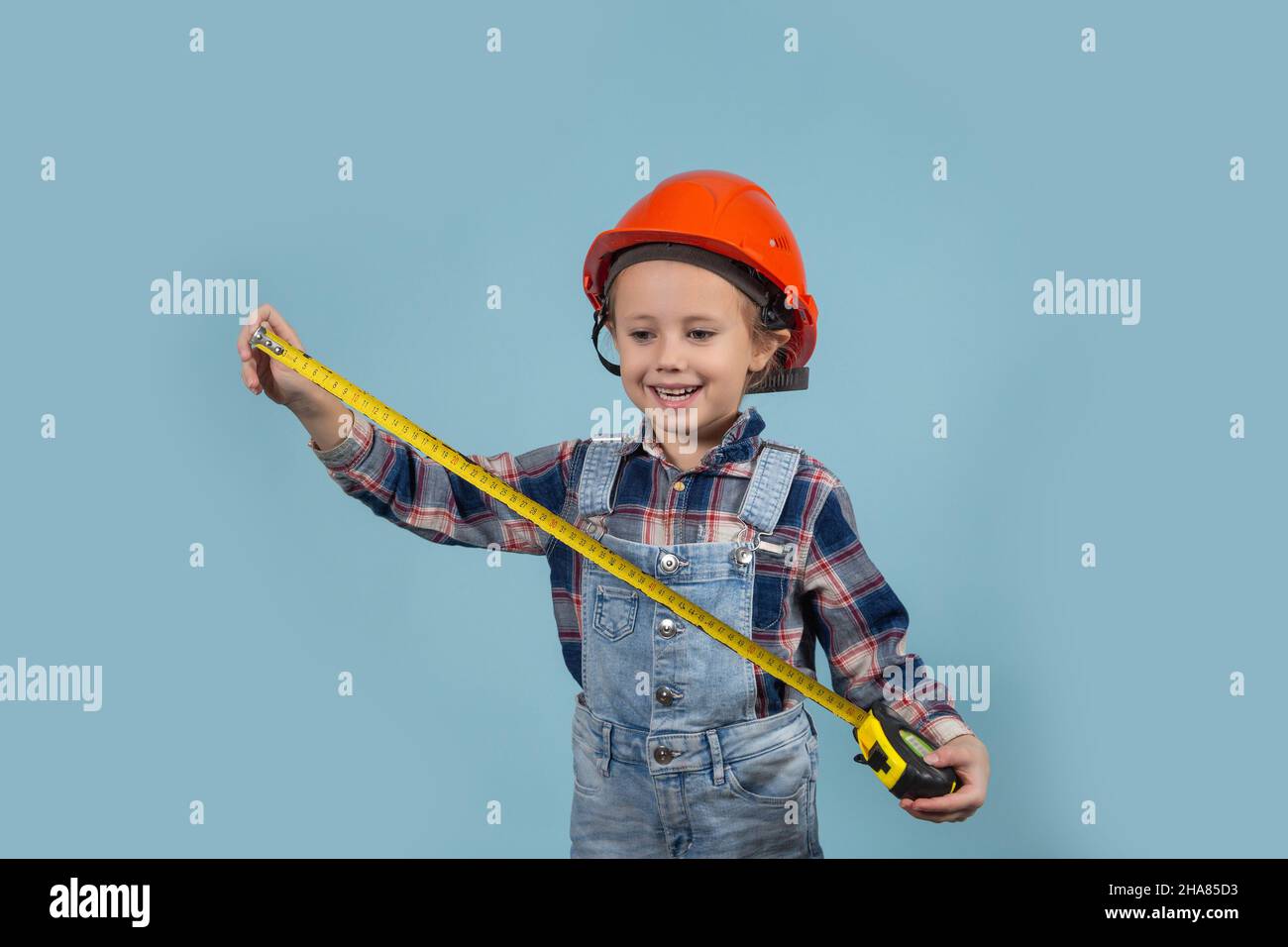 Portrait of adorable little caucasian kid wearing hard hat holding tape measure. Concept of Construction and repair. Stock Photo