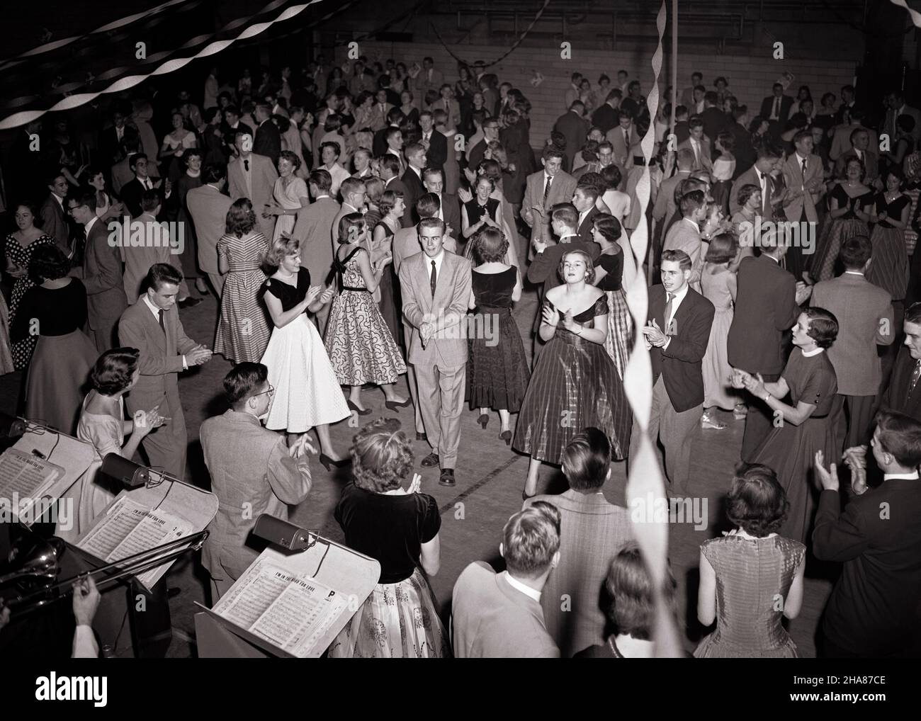 1950s TEENAGE BOYS IN SUITS AND GIRLS IN GOWNS DANCING CLAPPING HANDS IN FRONT OF BANDSTAND HIGH SCHOOL PROM DANCE PARTY - d1691 LAN001 HARS DANCERS SOCIAL OLD TIME NOSTALGIA OLD FASHION JUVENILE STYLE SUITS STRONG JOY LIFESTYLE CELEBRATION CROWDS FEMALES ASSEMBLY CLAPPING COPY SPACE FRIENDSHIP FULL-LENGTH HALF-LENGTH PERSONS CARING MALES TEENAGE GIRL TEENAGE BOY B&W GATHERING DATING SCHOOLS SUIT AND TIE HAPPINESS HIGH ANGLE AND EXCITEMENT GOWNS IN OF ATTRACTION GYMNASIUM HIGH SCHOOL BANDSTAND HIGH SCHOOLS COURTSHIP STYLISH TEENAGED IN FRONT OF PERSONAL ATTACHMENT POSSIBILITY AFFECTION EMOTION Stock Photo