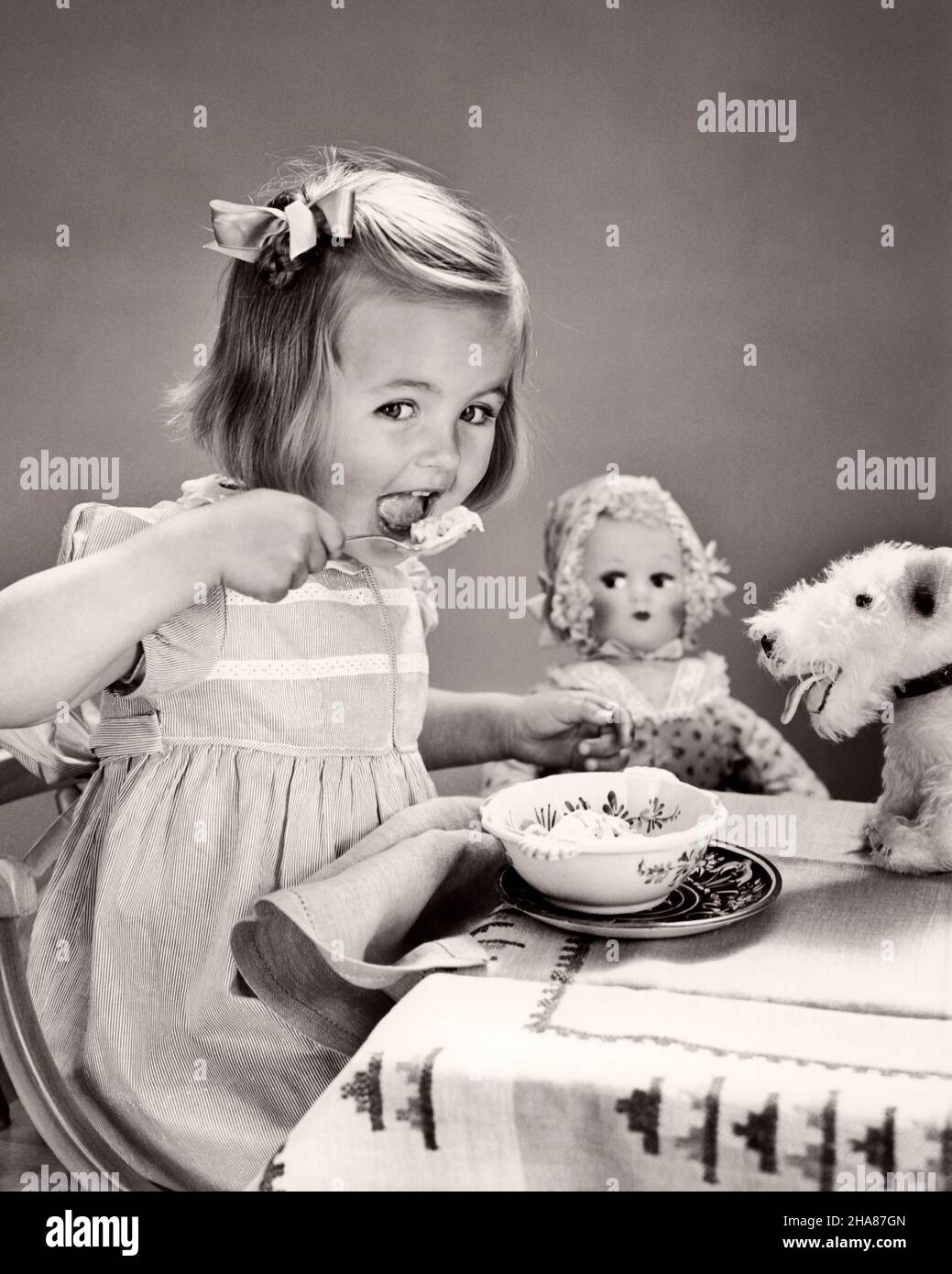 1940s GIRL LOOKING AT CAMERA BOW IN HER HAIR SITTING AT CHILD SIZED TABLE WITH DOLL AND STUFFED TOY DOG EATING BOWL OF ICE CREAM - f1471 HAR001 HARS FEMALES WINNING STUDIO SHOT STUFFED HEALTHINESS TREAT HOME LIFE COPY SPACE HALF-LENGTH B&W EYE CONTACT HUMOROUS HAPPINESS AND EXCITEMENT NUTRITION COMICAL COMEDY CONSUME CONSUMING NOURISHMENT ICE CREAM PLEASANT AGREEABLE CHARMING GROWTH JUVENILES LOVABLE PLEASING REFRESHING ADORABLE APPEALING BLACK AND WHITE CAUCASIAN ETHNICITY HAR001 OLD FASHIONED Stock Photo
