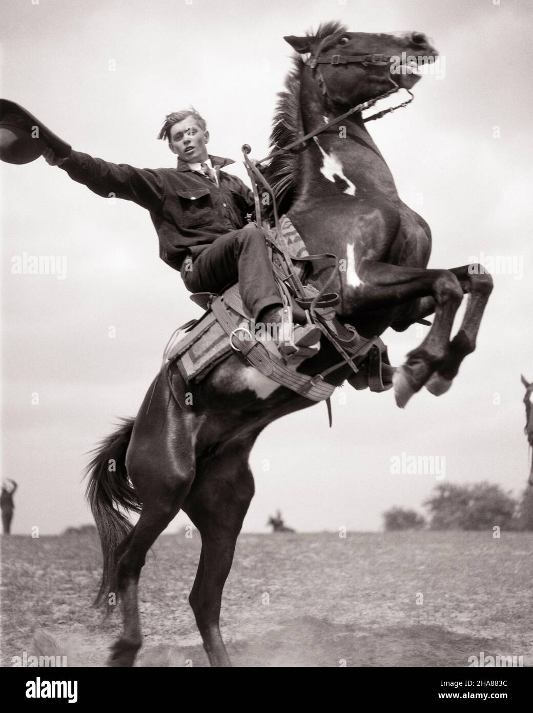 1920s YOUNG MAN RANCH HAND COWBOY ON WESTERN DUDE RANCH WAVING HAT DEMONSTRATING REARING A HORSE LOOKING AT CAMERA - h1144 HAR001 HARS BALANCE SAFETY TEAMWORK ATHLETE JOY LIFESTYLE ACTOR CELEBRATION JOBS RURAL ATHLETICS FULL-LENGTH PERSONS INSPIRATION SADDLE MALES RISK WESTERN ATHLETIC PERFORMANCE PROFESSION ENTERTAINMENT CONFIDENCE TRANSPORTATION B&W EYE CONTACT SUCCESS PERFORMING ARTS SKILL ACTIVITY DREAMS OCCUPATION PHYSICAL SKILLS MAMMALS REARING ADVENTURE PERFORMER STRENGTH COURAGE EXCITEMENT RECREATION PRIDE A ON DEMONSTRATION EMPLOYMENT ENTERTAINER OCCUPATIONS CONCEPTUAL ACTORS ATHLETES Stock Photo