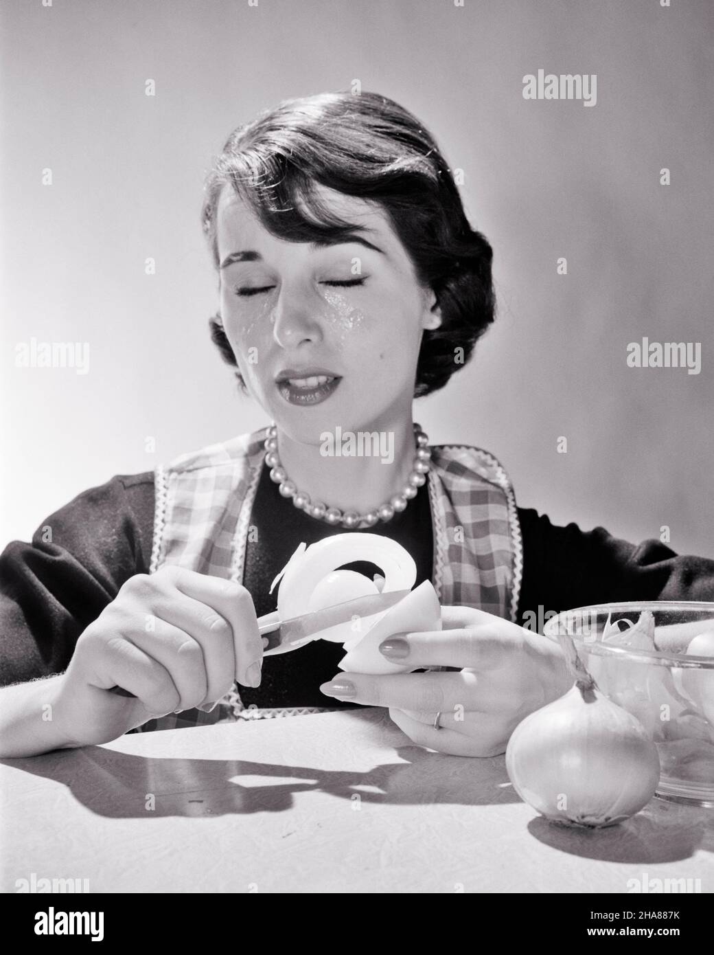 1950s 1960s WOMAN HOUSEWIFE COOK REACTING TO PEELING ONION CRYING TEARS WATERING BURNING SENSATION EYES CLOSED - h2828 DEB001 HARS CHEMISTRY FEMALES STUDIO SHOT GROWNUP TEARS HOME LIFE PREPARING COPY SPACE LADIES PERSONS GROWN-UP CRY B&W BRUNETTE HOMEMAKER PEOPLE STORY HOMEMAKERS HEAD AND SHOULDERS ONION HOUSEWIVES IRRITATION NOURISHMENT STYLISH ACID DEB001 IRRITANT REACTING SENSATION PEELING CHEMICAL REACTION EMOTION EMOTIONAL EMOTIONS MID-ADULT MID-ADULT WOMAN REACTION STINGING SULFUR YOUNG ADULT WOMAN BLACK AND WHITE CAUCASIAN ETHNICITY OLD FASHIONED ONIONS Stock Photo