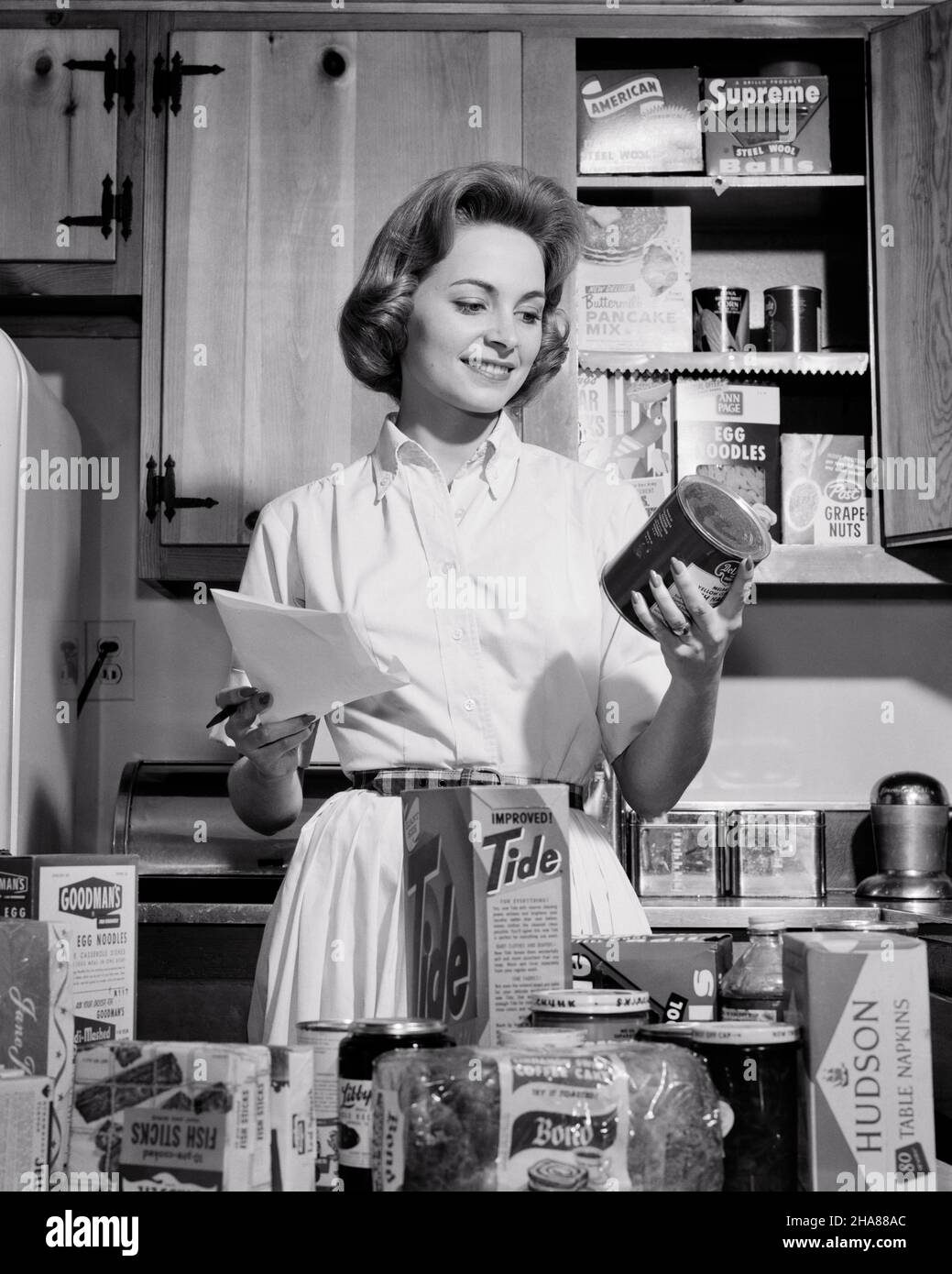 1960s 1950s SMILING WOMAN HOUSEWIFE IN KITCHEN WEARING SHIRTWAIST DRESS CHECKING HER GROCERY DELIVERY AGAINST HER SHOPPING LIST - h3041 DEB001 HARS CHORES FEMALES HOME LIFE COPY SPACE AGAINST HALF-LENGTH LADIES PERSONS CARING CONFIDENCE EXPRESSIONS B&W SHOPPER HOMEMAKER SHOPPERS HOMEMAKERS CHEERFUL CHORE CHOICE HOUSEWIVES SMILES SHIRTWAIST TASKS CONCEPTUAL JOYFUL DEB001 MID-ADULT MID-ADULT WOMAN TASK BLACK AND WHITE CAUCASIAN ETHNICITY OLD FASHIONED PURCHASES Stock Photo