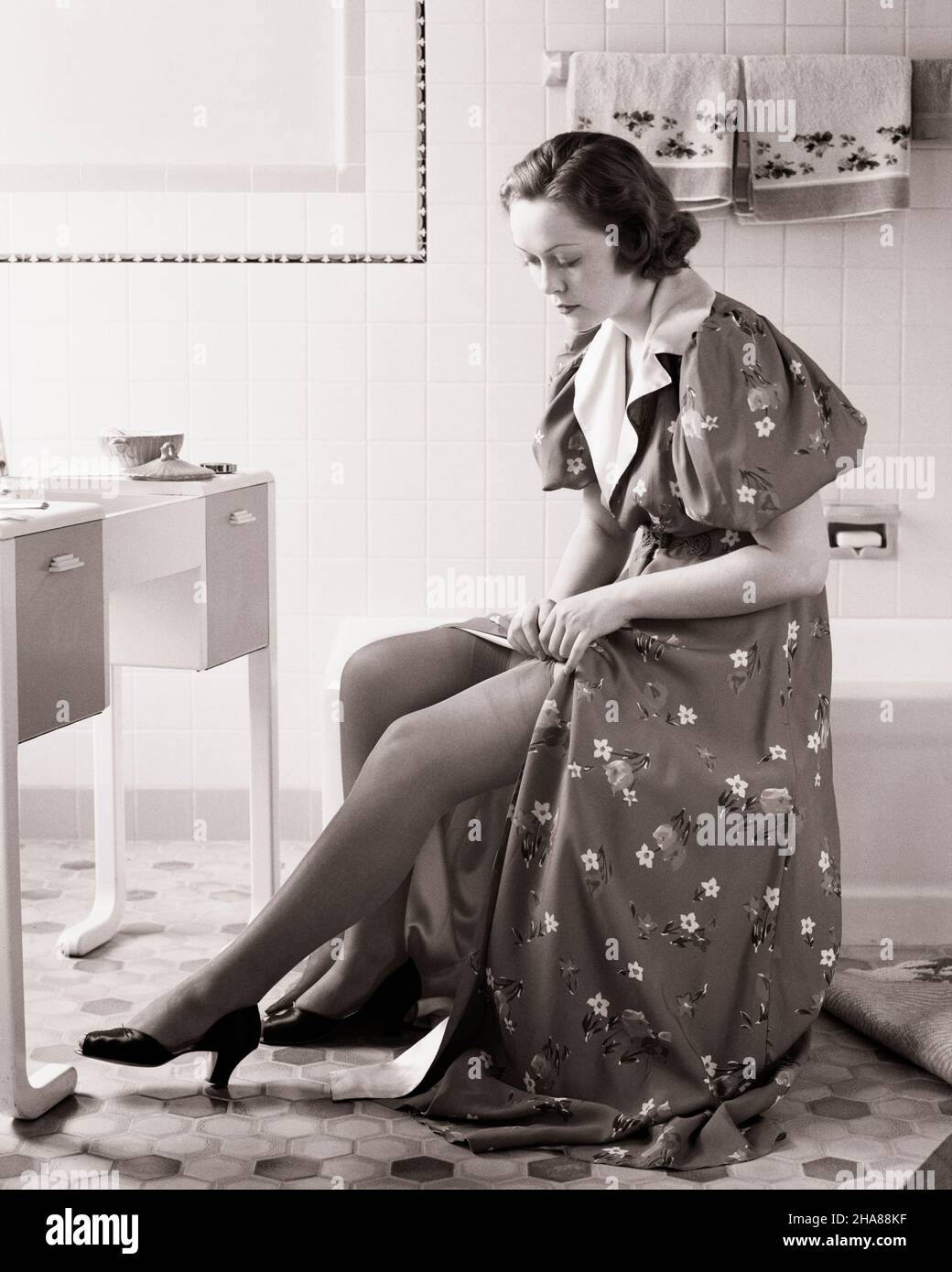 1930s-1940s-woman-sitting-at-bathroom-vanity-putting-on-pair-of