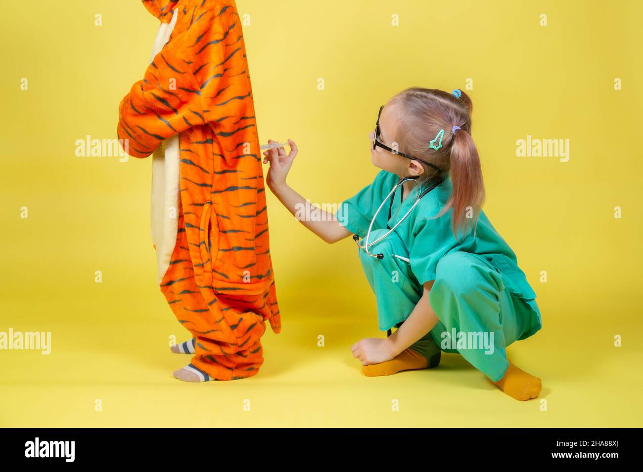 Little caucasian Children play doctor, a girl dressed as a doctor gives an injection to a boy dressed as a tiger Stock Photo