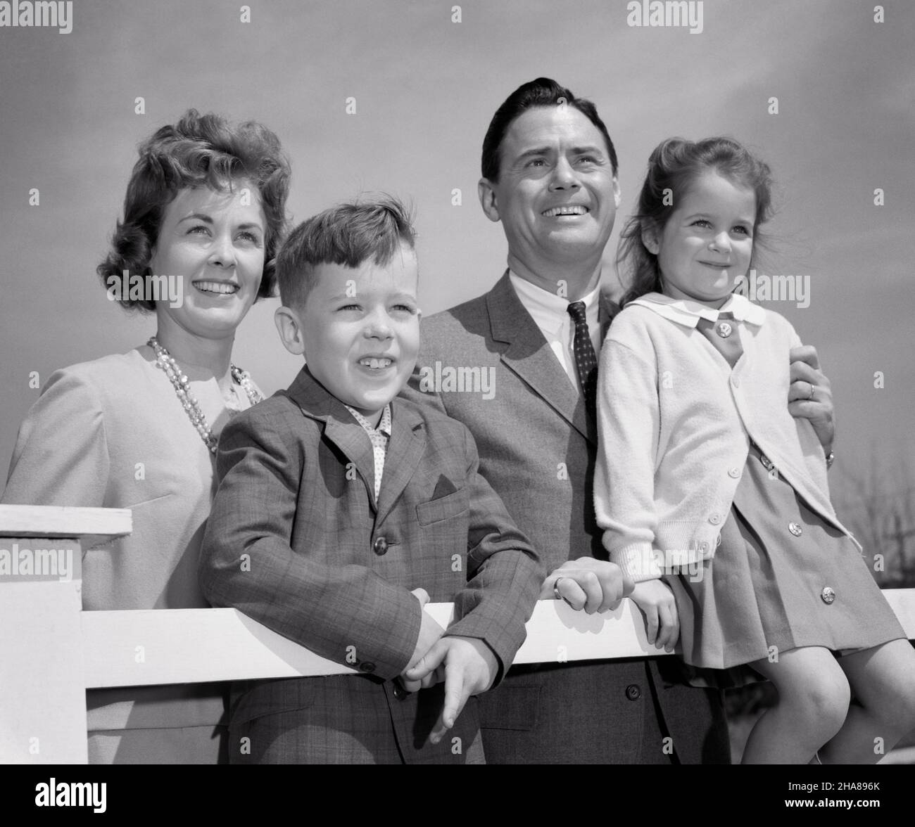 1960s PORTRAIT OF SMILING FAMILY OF FOUR MOTHER FATHER TWO KIDS A BOY AND GIRL LEANING ON FENCE LOOKING PAST CAMERA - j1334 HAR001 HARS BEAUTY COMMUNITY SUBURBAN URBAN MOTHERS MAGIC OLD TIME NOSTALGIA BROTHER OLD FASHION SISTER 1 JUVENILE BALANCE SAFETY SONS PLEASED FAMILIES JOY LIFESTYLE SATISFACTION CELEBRATION FEMALES MARRIED BROTHERS SPOUSE HUSBANDS HEALTHINESS HOME LIFE COPY SPACE HALF-LENGTH LADIES PHYSICAL FITNESS DAUGHTERS PERSONS INSPIRATION CARING MALES SERENITY SIBLINGS SPIRITUALITY CONFIDENCE SISTERS FATHERS B&W PARTNER SUCCESS DREAMS HAPPINESS WELLNESS CHEERFUL LEISURE STRENGTH Stock Photo