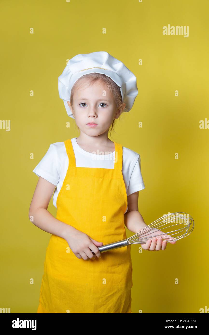 Girl in apron and chef's hat holding a whisk for whipping cream Stock Photo
