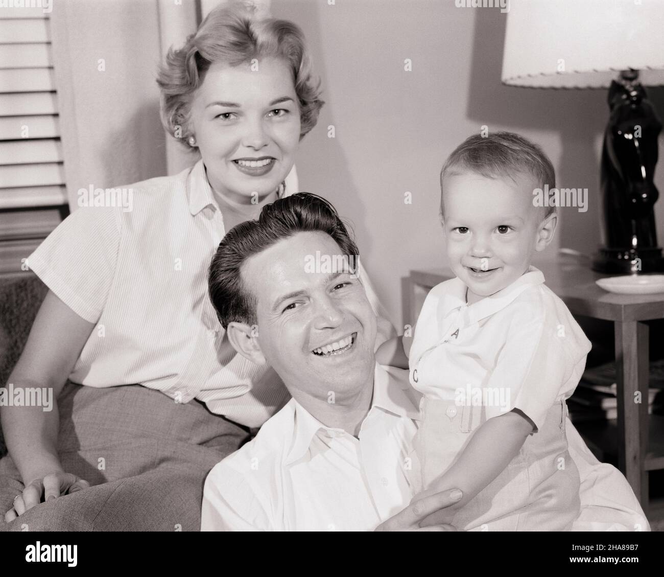 1950s PORTRAIT OF SMILING FAMILY OF THREE MOTHER FATHER TODDLER BOY LOOKING AT CAMERA SITTING IN LIVING ROOM - j5390 HAR001 HARS BEAUTY SUBURBAN URBAN MOTHERS OLD TIME FUTURE NOSTALGIA OLD FASHION 1 JUVENILE YOUNG ADULT BALANCE TEAMWORK SONS PLEASED FAMILIES JOY LIFESTYLE SATISFACTION CELEBRATION FEMALES MARRIED SPOUSE HUSBANDS HEALTHINESS HOME LIFE COPY SPACE HALF-LENGTH LADIES PERSONS INSPIRATION CARING MALES CONFIDENCE FATHERS B&W PARTNER EYE CONTACT SUCCESS DREAMS HAPPINESS WELLNESS CHEERFUL STRENGTH LIVING ROOM DADS PRIDE AUTHORITY SMILES CONNECTION JOYFUL STYLISH MIDDLE CLASS GROWTH Stock Photo