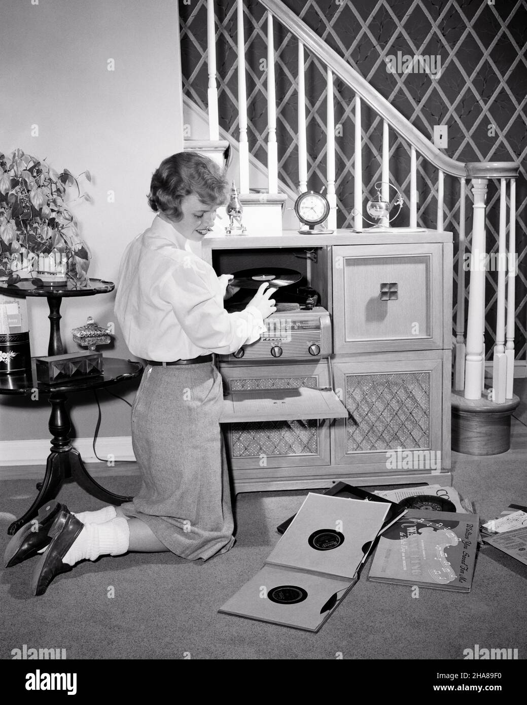 1950s TEENAGE GIRL WEARING SHIRT SKIRT BOBBY SOCKS LOAFERS KNEELING BY CONSOLE RADIO PHONOGRAPH PLAYING 78 RPM VINYL RECORDS - j5793 HAR001 HARS JUVENILE STYLE COMMUNICATION RECORDS VINYL JOY LIFESTYLE SOUND CELEBRATION FEMALES HOUSES HOME LIFE COPY SPACE FULL-LENGTH PERSONS INSPIRATION RESIDENTIAL TEENAGE GIRL BUILDINGS ENTERTAINMENT B&W PHONOGRAPH KNEELING CONSOLE HAPPINESS LEISURE CHOICE EXCITEMENT KNOWLEDGE RECREATION OPPORTUNITY HOMES 78 RPM CONCEPTUAL LOAFERS BOBBY RESIDENCE STYLISH TEENAGED WHITE BLOUSE JUVENILES RELAXATION WEARING  BLACK AND WHITE CAUCASIAN ETHNICITY HAR001 KNEEL Stock Photo