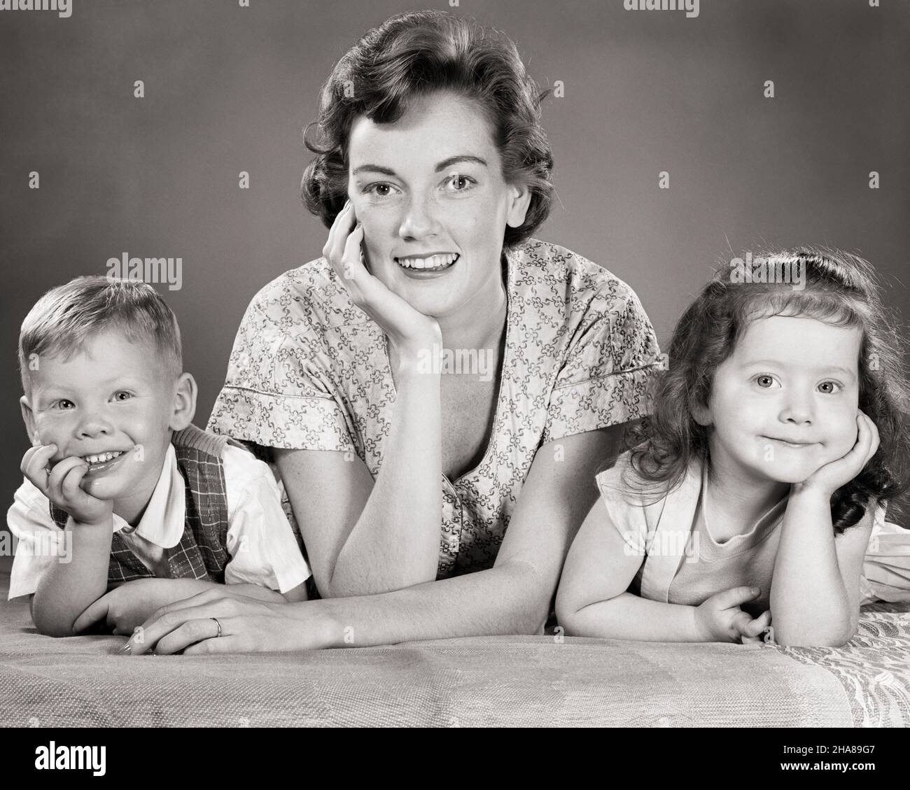 1950s PORTRAIT SMILING WOMAN MOTHER AND BOY SON BROTHER AND GIRL DAUGHTER SISTER ALL LEANING ON ELBOWS LOOKING AT CAMERA - j6308 HAR001 HARS 1 JUVENILE YOUNG ADULT TEAMWORK SONS PLEASED FAMILIES JOY LIFESTYLE FEMALES BROTHERS HEALTHINESS HOME LIFE COPY SPACE FRIENDSHIP LADIES DAUGHTERS PERSONS MALES ALL SIBLINGS SISTERS B&W EYE CONTACT HAPPINESS HEAD AND SHOULDERS CHEERFUL AND ON SIBLING SMILES ELBOWS CONNECTION JOYFUL COOPERATION JUVENILES MOMS TOGETHERNESS YOUNG ADULT WOMAN BLACK AND WHITE CAUCASIAN ETHNICITY HAR001 OLD FASHIONED Stock Photo
