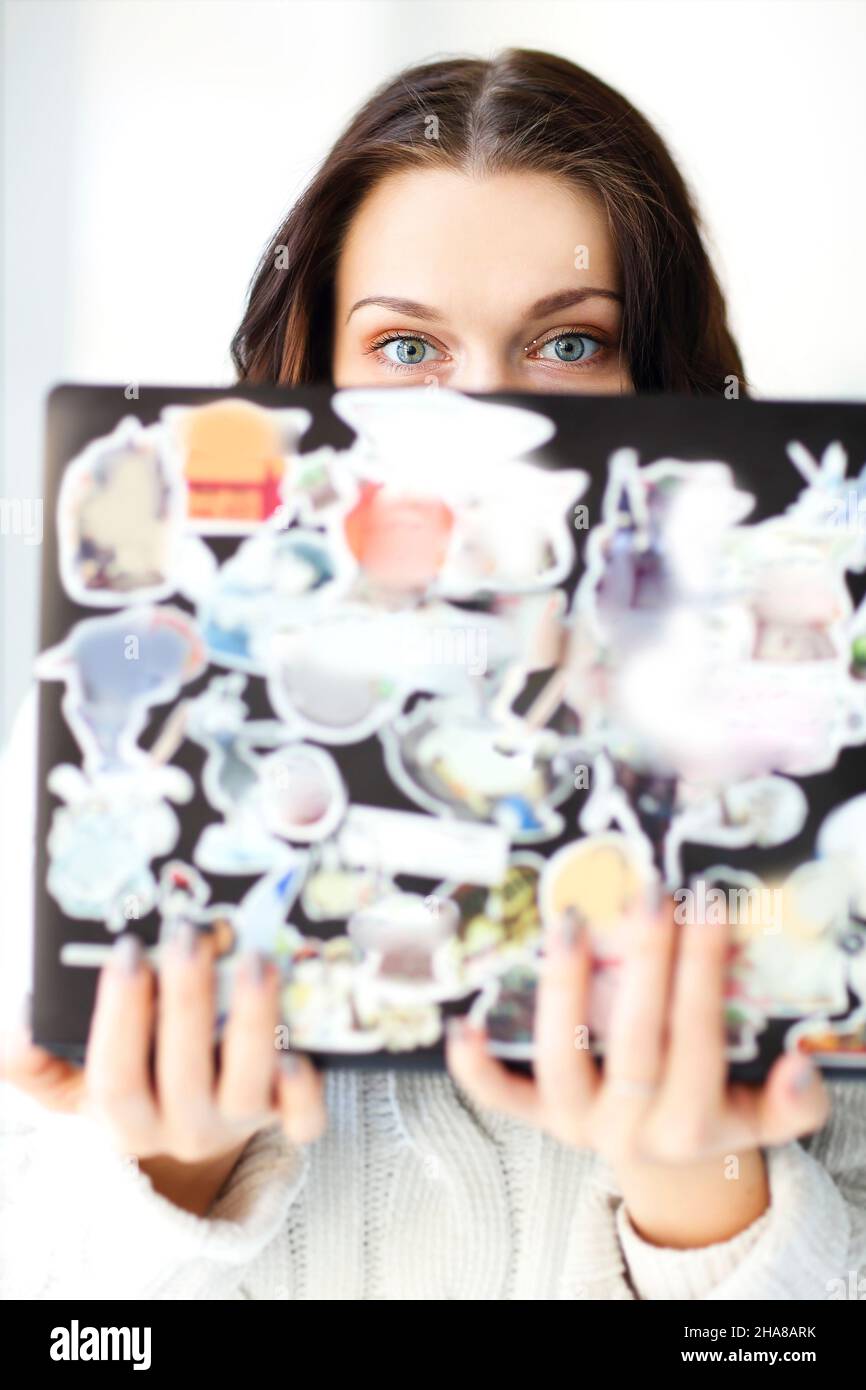 Close up photo of caucasian brunette girl holding open laptop in hands while looking over computer screen into camera with round big shocked blue eyes Stock Photo