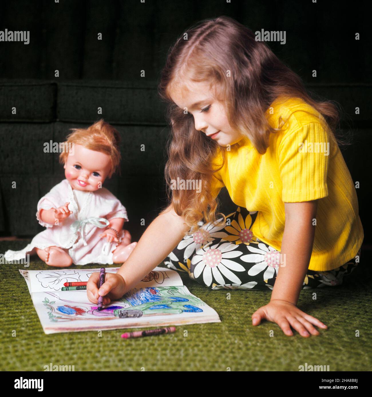 1970s LITTLE GIRL SITTING ON FLOOR WITH HER DOLL COLORING IN COLORING BOOK WITH CRAYONS WEARING YELLOW TOP AND DAISY PRINT PANTS - kj4550 HAR001 HARS HEALTHINESS HOME LIFE COPY SPACE HALF-LENGTH DAISY HAPPINESS AND CRAYONS COLORING BOOK CONTENT IMAGINATION CALM PLEASANT AGREEABLE CHARMING CREATIVITY JUVENILES LOVABLE PLEASING ADORABLE APPEALING CAUCASIAN ETHNICITY COLORING HAR001 OLD FASHIONED Stock Photo