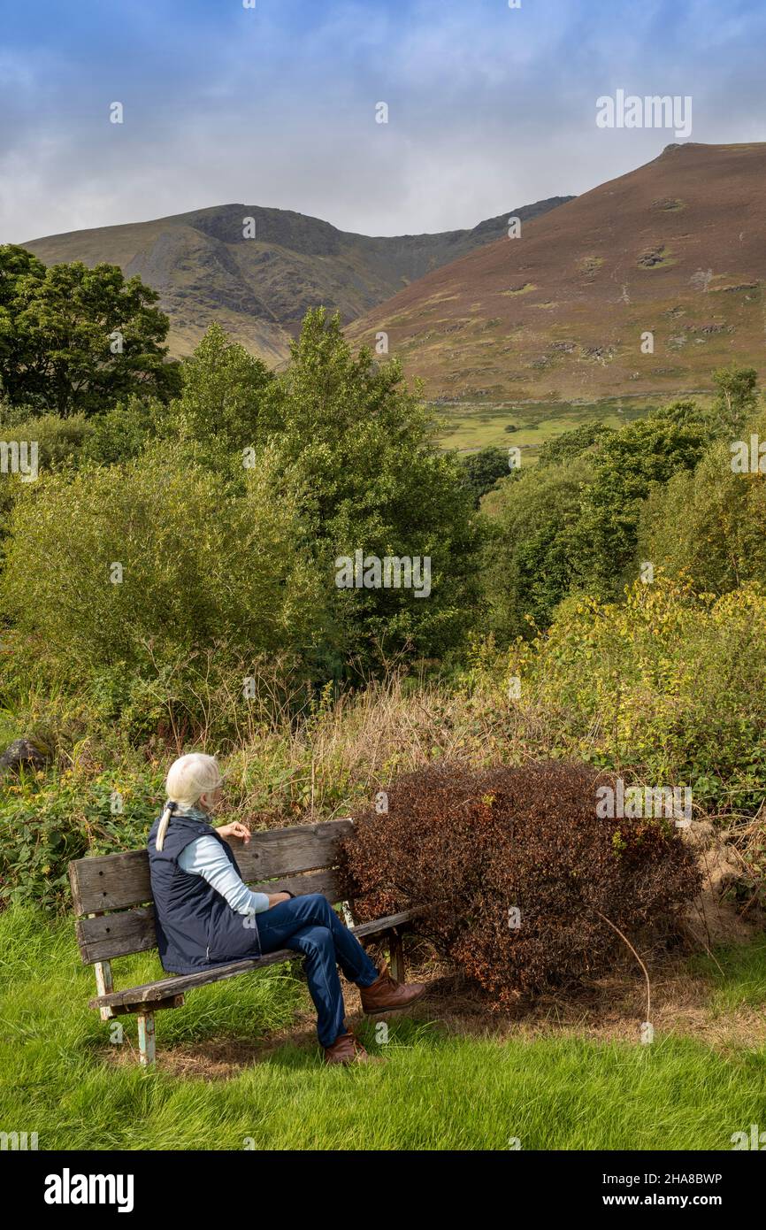 UK, Cumbria, Allerdale, Keswick, Threlkeld, tourist sat on public bench below Blencathra ‘Saddleback’ hill Stock Photo