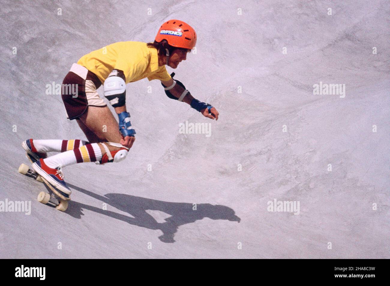 1980s YOUNG MAN SKATEBOARDING IN SKATE PARK WEARING HELMET KNEE AND SHOULDER PADS CASTING A