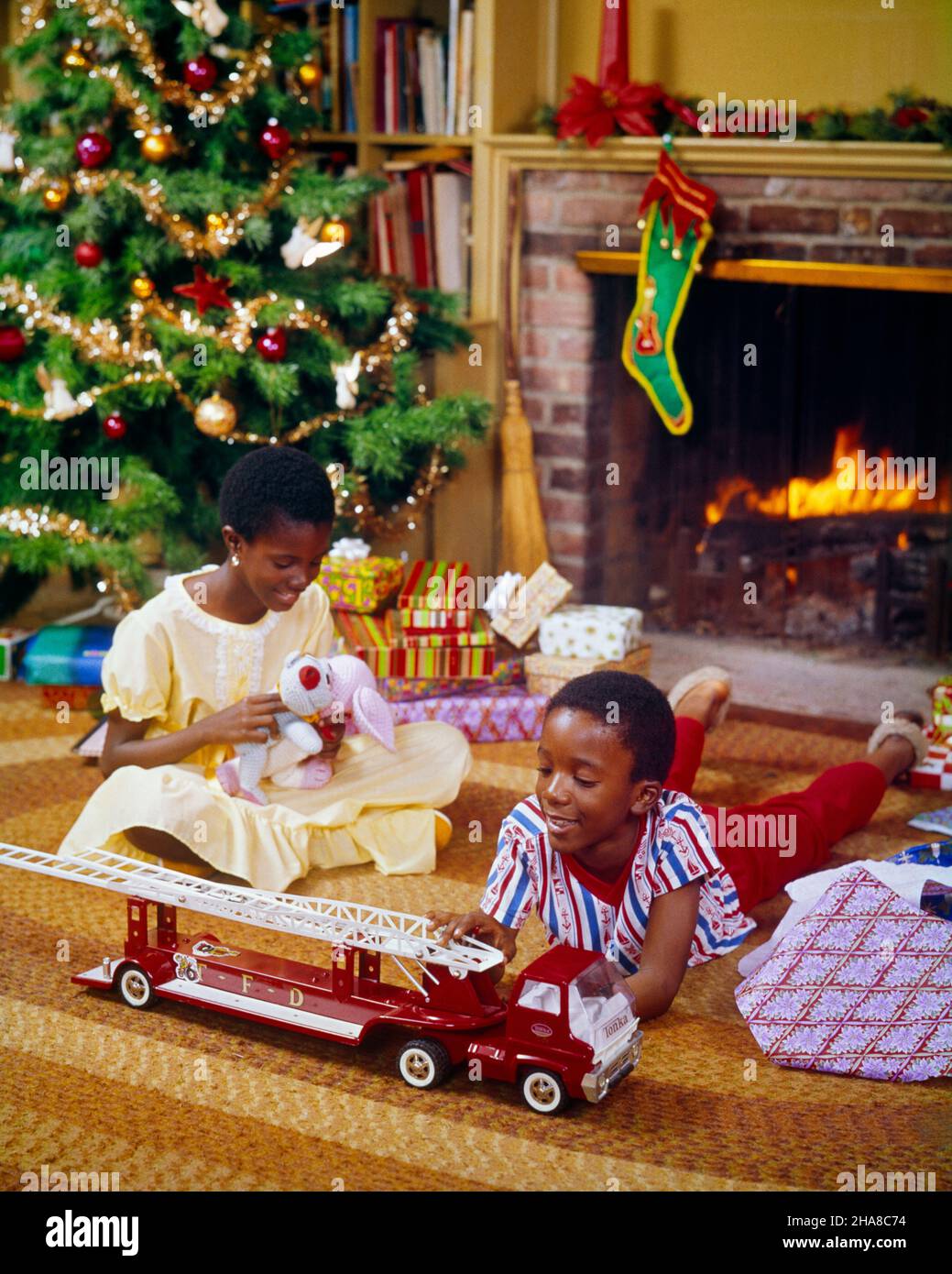 1970s AFRICAN-AMERICAN BROTHER AND SISTER BY CHRISTMAS TREE AND FIREPLACE GIRL HOLD STUFFED DOG TOY AND BOY WITH TOY FIRE TRUCK - kx7399 PHT001 HARS JOY LIFESTYLE SATISFACTION CELEBRATION FEMALES BROTHERS STUFFED HEALTHINESS HOME LIFE COPY SPACE HALF-LENGTH PERSONS MALES SIBLINGS SISTERS MORNING HAPPINESS HIGH ANGLE AFRICAN-AMERICANS MERRY AFRICAN-AMERICAN AND EXCITEMENT BLACK ETHNICITY SIBLING DECEMBER CONNECTION DECEMBER 25 IMAGINATION COOPERATION JOYOUS JUVENILES TOGETHERNESS OLD FASHIONED AFRICAN AMERICANS Stock Photo