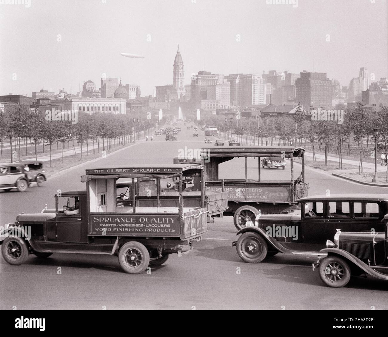 1920s 1930s CAR AND TRUCK TRAFFIC AROUND THE ART MUSEUM VIEW TOWARDS DOWNTOWN SKYLINE BLIMP IN SKY PHILADELPHIA PA USA - p2881 HAR001 HARS STRUCTURES AUTOMOBILES BENJAMIN FRANKLIN PARKWAY CITIES KEYSTONE STATE VEHICLES AIRSHIP EDIFICE DIRIGIBLE BLACK AND WHITE CITY OF BROTHERLY LOVE HAR001 OLD FASHIONED Stock Photo