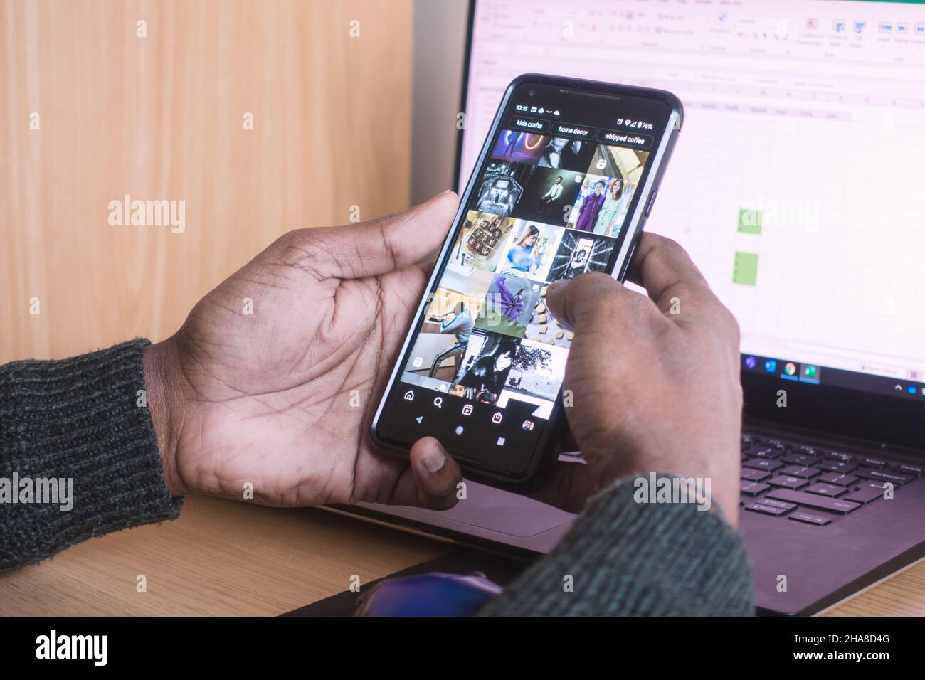 Adult male hands holding smartphone and checking social media Instagram with a Laptop in background as a concept of work distraction Stock Photo