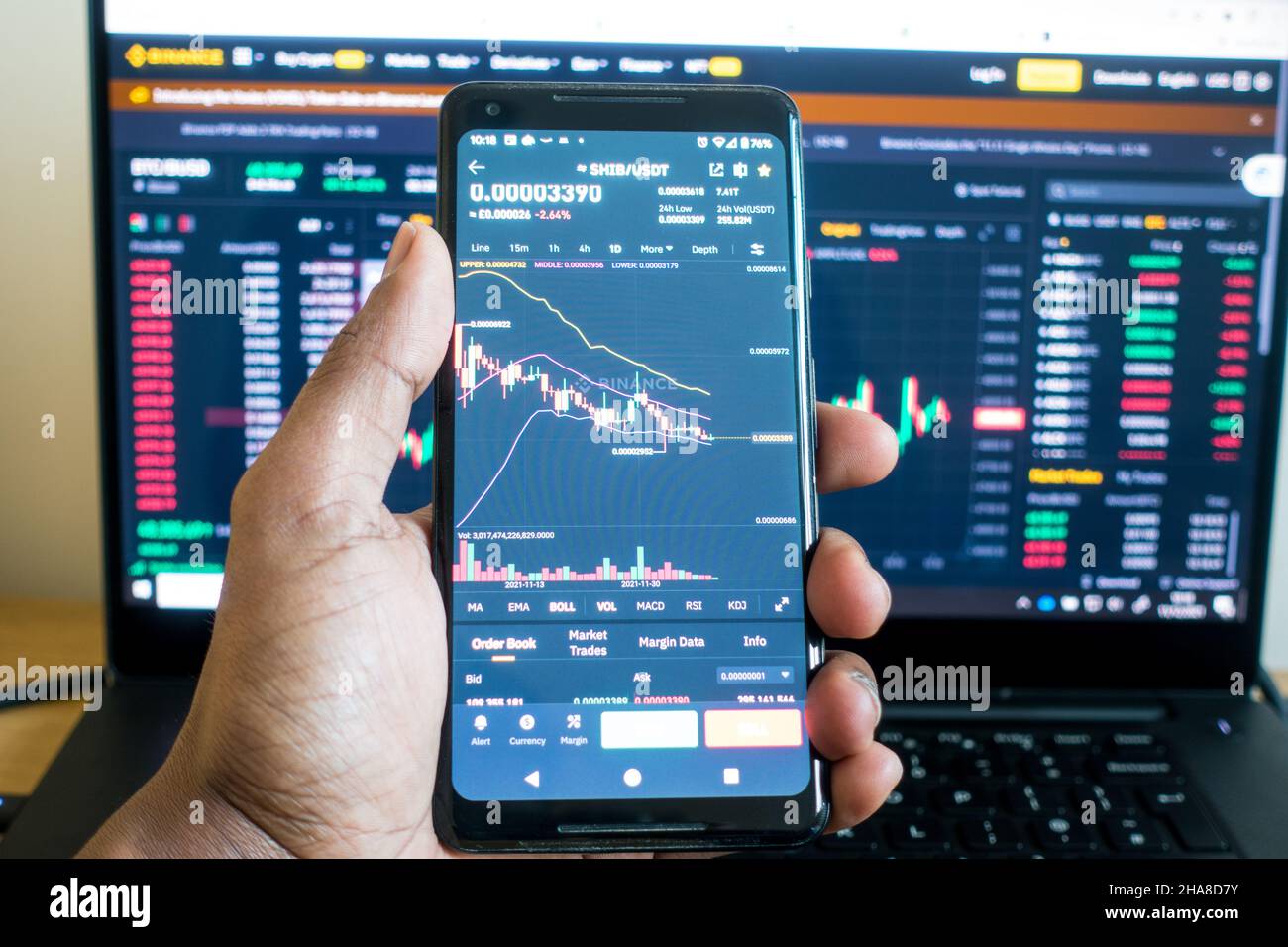 Adult male watching crypto charts on mobile and a laptop screen in background Stock Photo