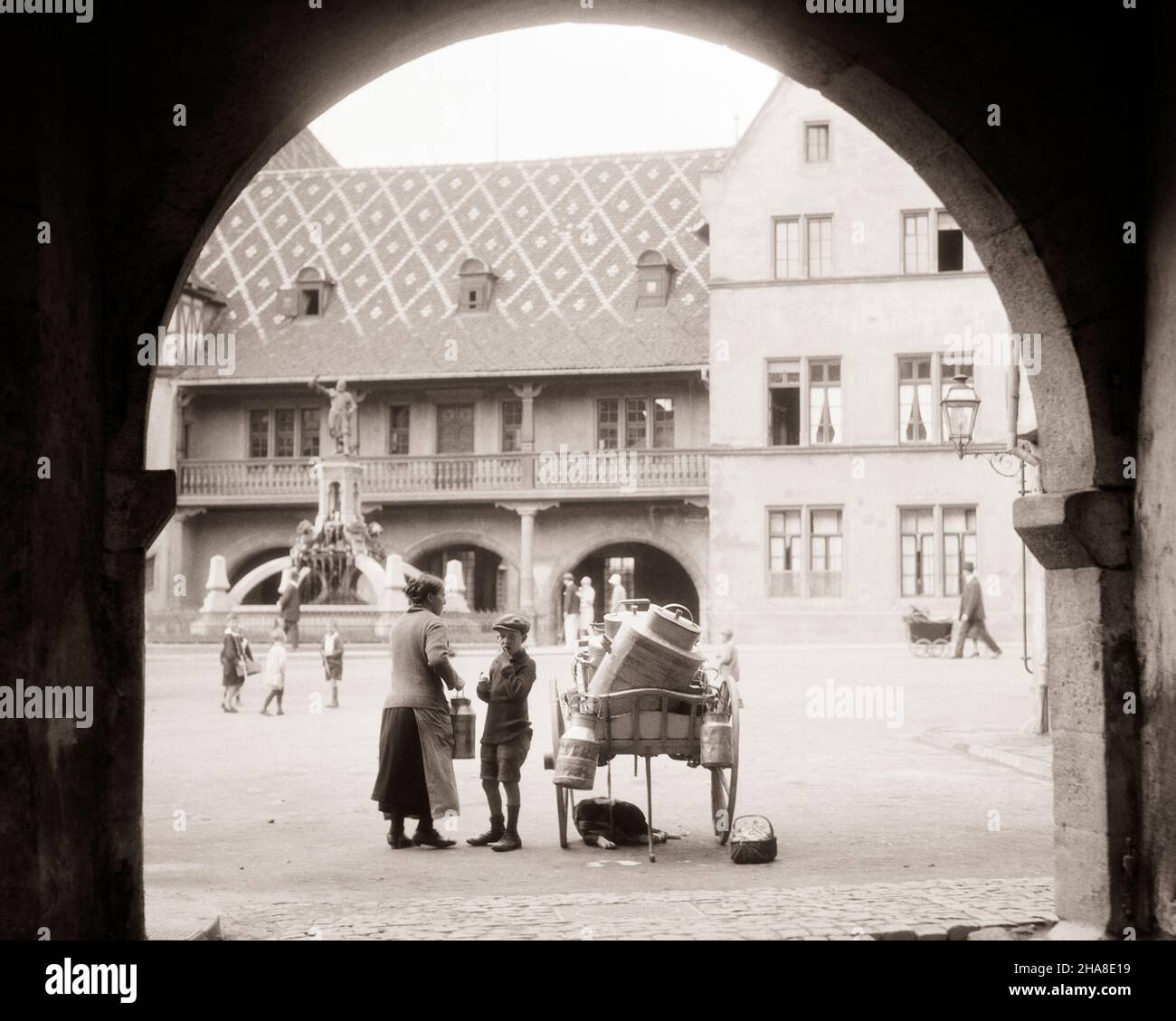 1920s 1930s WOMAN AND BOY BY MILK WAGON CART COLMAR ALSACE FRANCE WITH ANCIENNE DOUANE OLD CUSTOMS HOUSE IN BACKGROUND - r2687 HAR001 HARS DAIRY COPY SPACE FULL-LENGTH LADIES PERSONS MALES BUILDINGS EUROPE B&W STRUCTURE WELLNESS BEVERAGE EUROPEAN PROPERTY AND EXTERIOR FLUID ALSACE REAL ESTATE STRUCTURES EDIFICE CUSTOMS GROWTH JUVENILES PROTEIN BEVERAGES BLACK AND WHITE HAR001 OLD FASHIONED Stock Photo