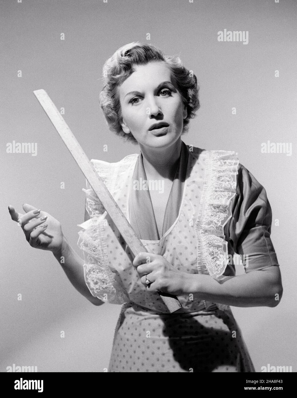1950s 1960s SERIOUS HOUSEWIFE MOTHER WEARING APRON LOOKING AT CAMERA HOLDING YARD STICK STRESSING A POINT OF ORDER OR DISCIPLINE - s4338 CLE003 HARS HALF-LENGTH LADIES PERSONS DISCIPLINE TROUBLED B&W CONCERNED SADNESS EYE CONTACT HOMEMAKER HOMEMAKERS STRATEGY RULER POWERFUL A AUTHORITY HOUSEWIVES MOOD CONCEPTUAL GLUM OR MID-ADULT MID-ADULT WOMAN MISERABLE SOLUTIONS STRESSING YARD STICK BLACK AND WHITE CAUCASIAN ETHNICITY OLD FASHIONED Stock Photo