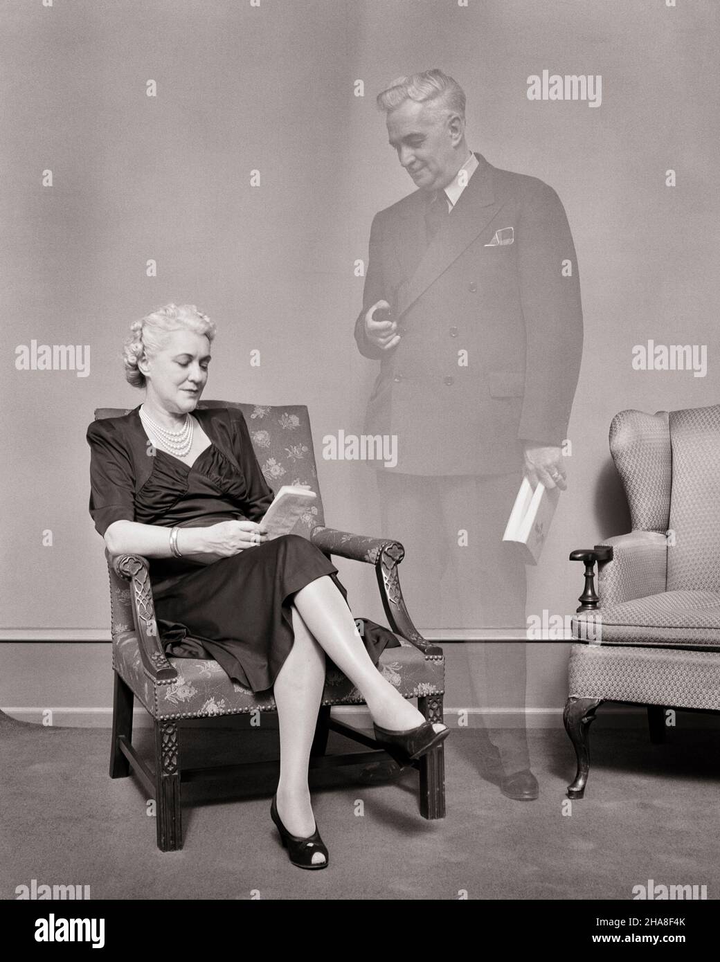 1940s WIDOWED SENIOR WOMAN SITTING IN CHAIR READING WITH SPIRIT OF HER DEAD HUSBAND GHOSTED STANDING BESIDE HER - s4829 HAR001 HARS HAUNTED COPY SPACE LADIES PERSONS INSPIRATION CARING MALES SPIRITUALITY SENIOR MAN DEAD SENIOR ADULT B&W PARTNER SENIOR WOMAN DREAMS SPIRIT OLD AGE OLDSTERS OLDSTER ELDERS CONNECTION WIDOW PHANTOM BESIDE IMAGINATION SUPPORT GHOSTED PANORAMIC PERSONAL ATTACHMENT AFFECTION EMOTION WIDOWED WIVES BLACK AND WHITE CAUCASIAN ETHNICITY HAR001 OLD FASHIONED Stock Photo