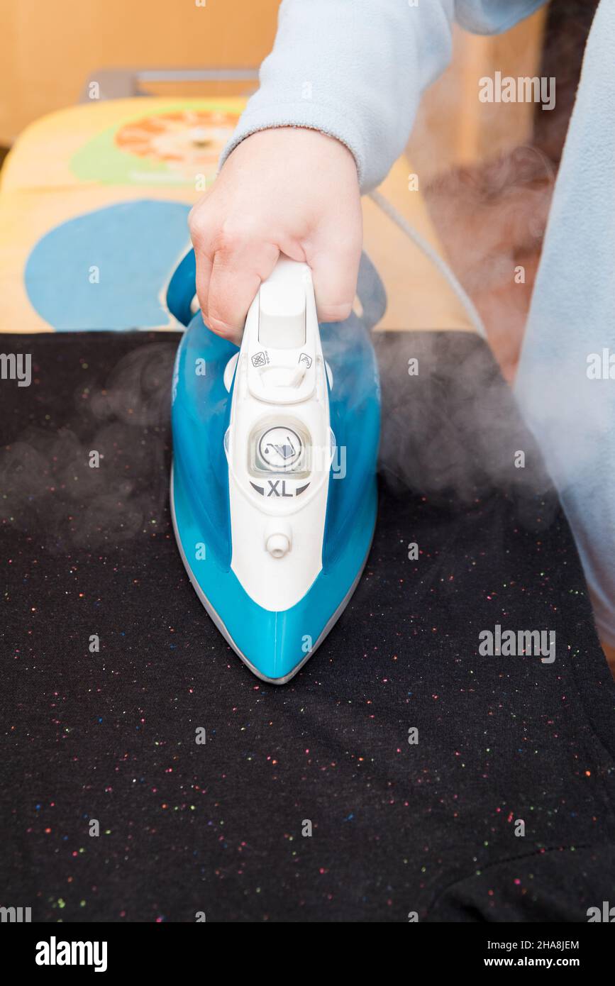 Vertical photo of a Woman ironing a black Tshirt on an ironing board as seen from above Stock
