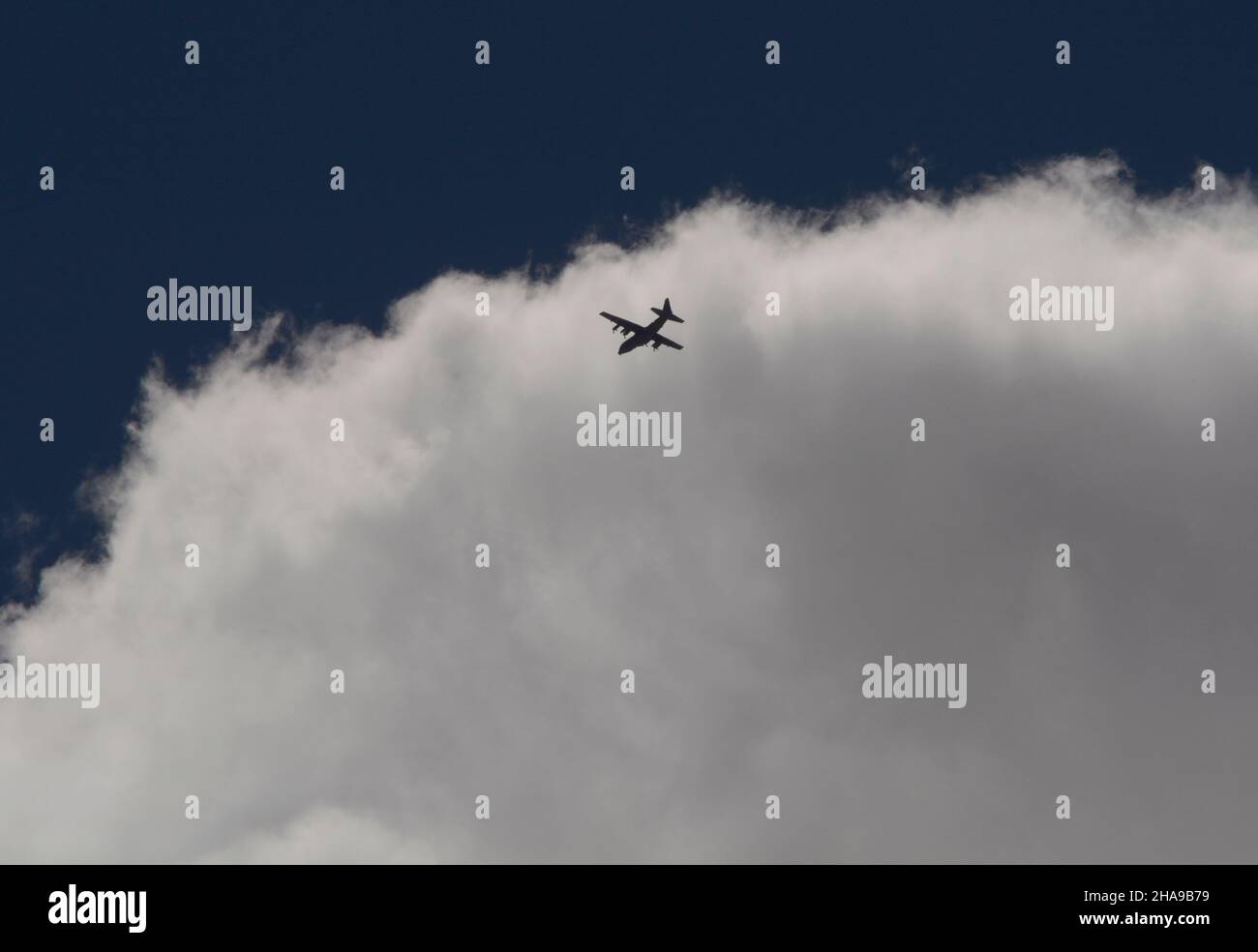 A Lockheed C130 Hercules military cargo aircraft flies through clouds
