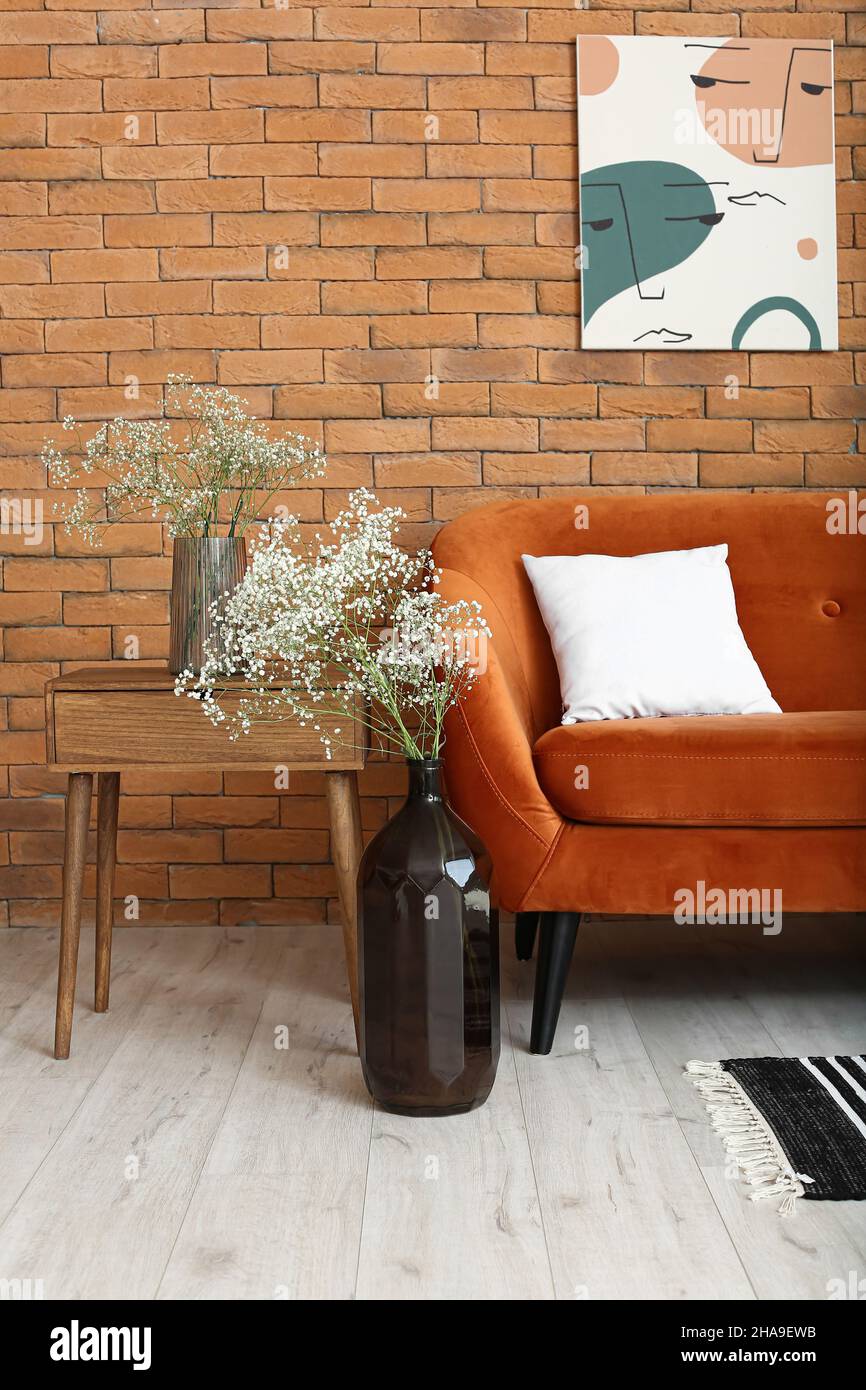 Vases with gypsophila flowers, table and sofa near brick wall Stock ...