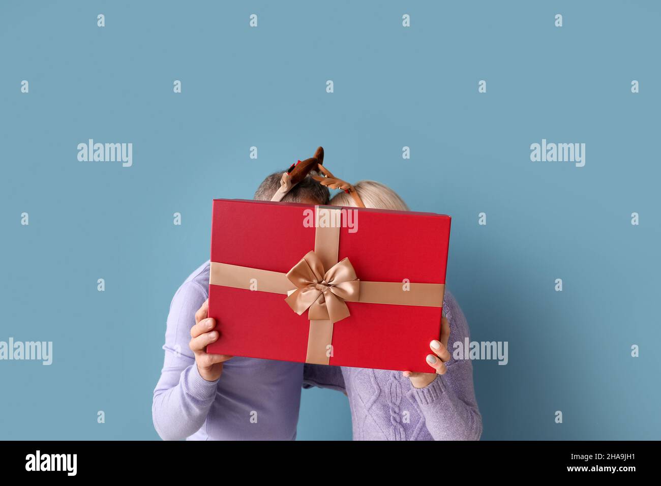 Happy mature couple with Christmas gift on color background Stock Photo