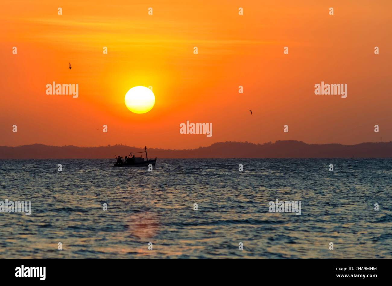 Sunset seen from Ribeira beach in Salvador, Bahia, Brazil. A boat sails at sea. Stock Photo