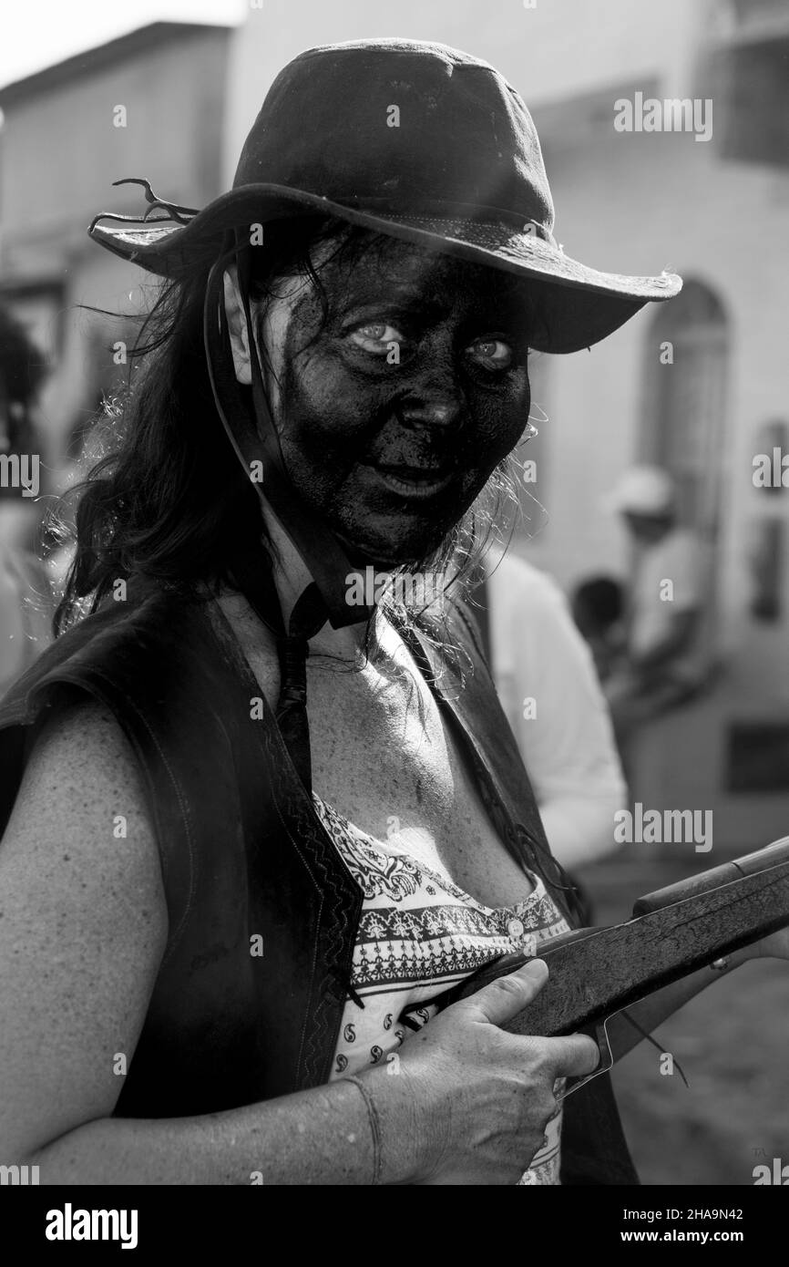 Caucasian woman with face made up in black color. She is wearing a pink hat and holding a brown colored gun. Acupe, Bahia, Brazil. Stock Photo