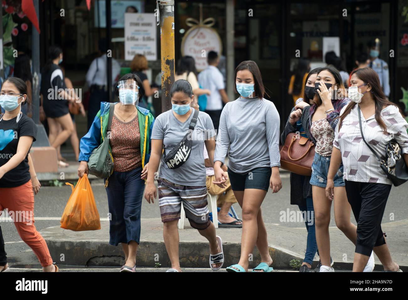 People in the Philippines crossing a road wearing face masks with one woman also wearing a face shield. Stock Photo