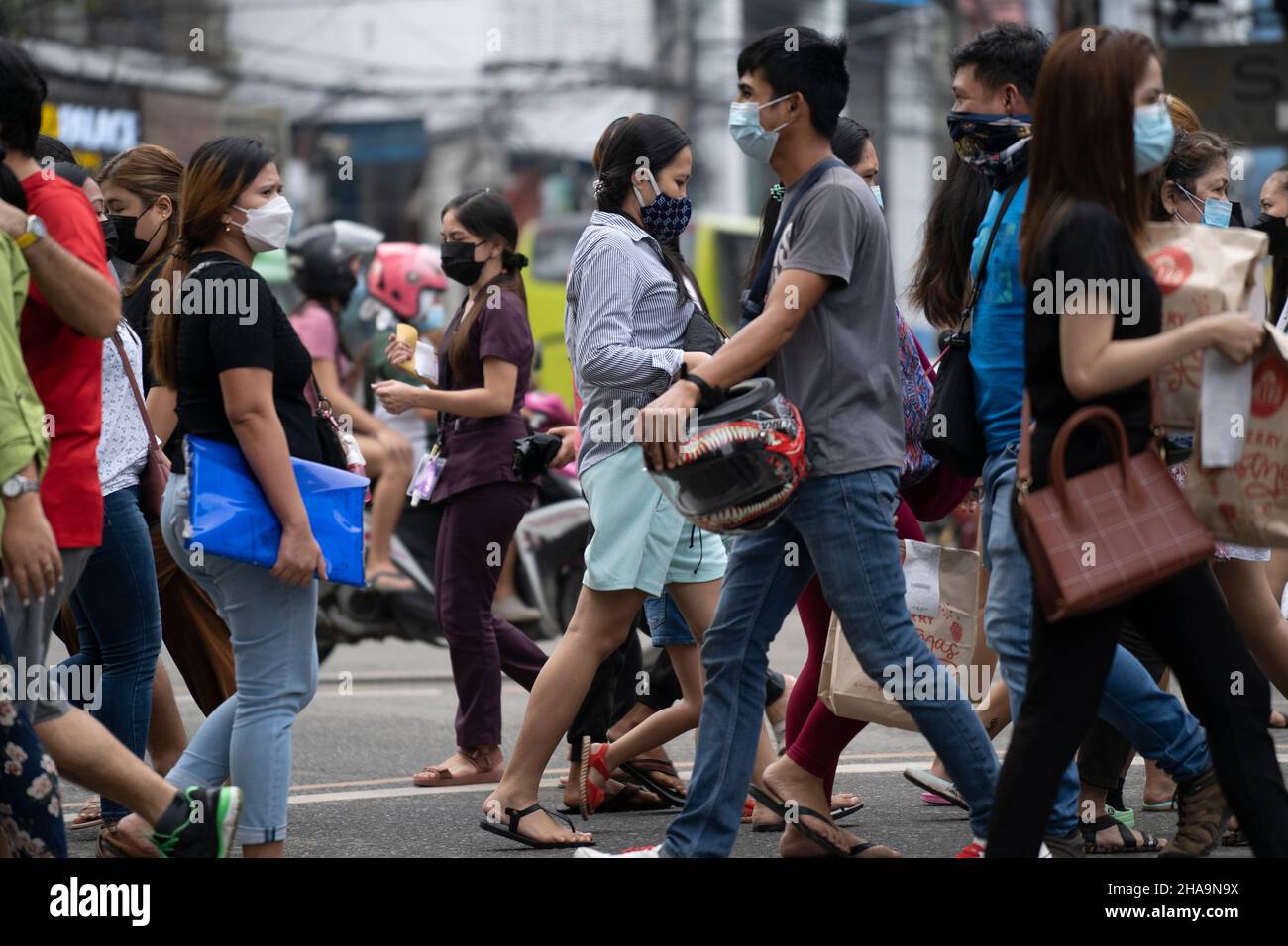 People in the Philippines crossing a road wearing face masks, the wearing of face masks in public places and establishments is mandatory. Stock Photo