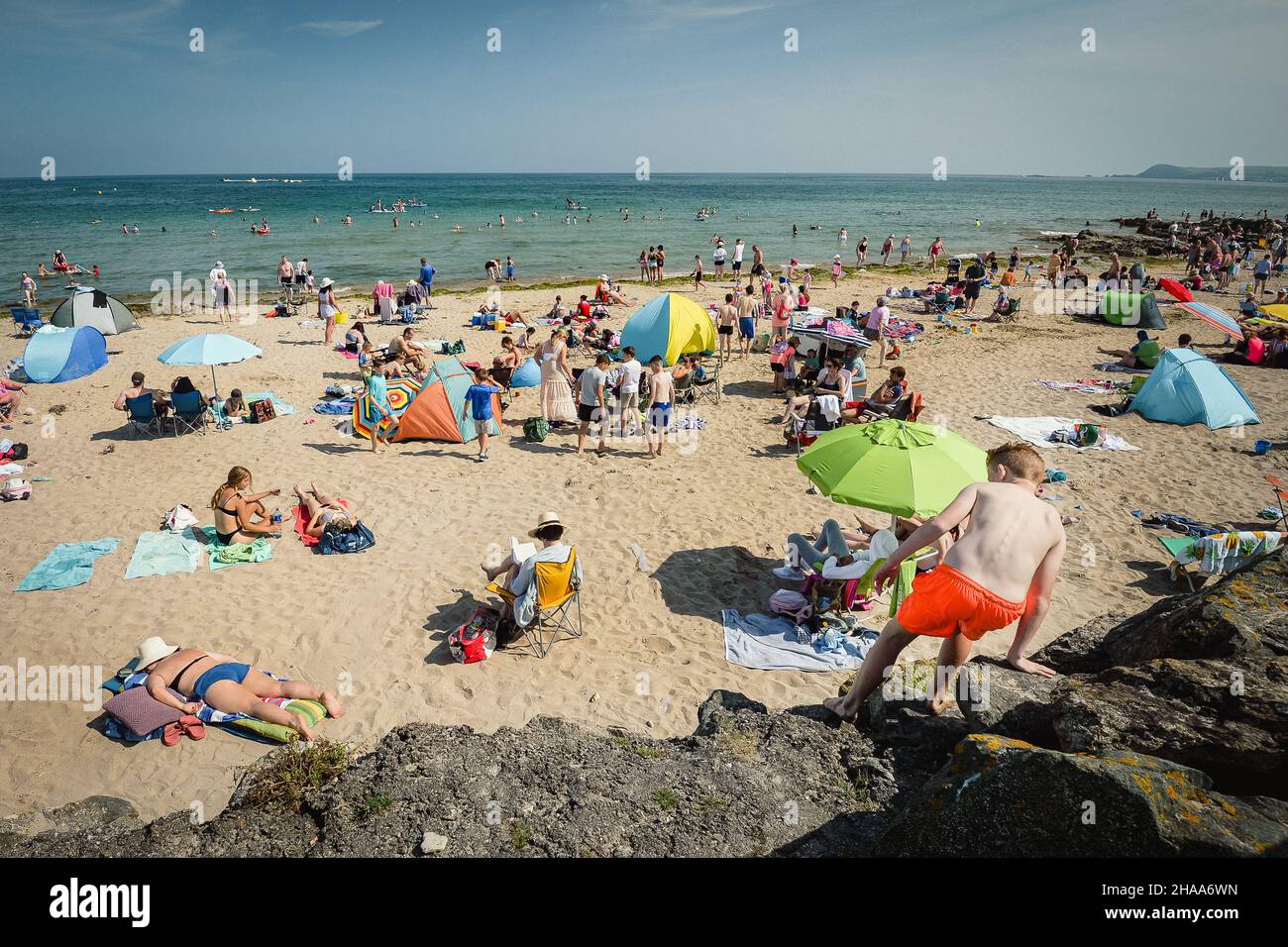 Boy climbing rocks at a busy Clonea Strand beach, County Waterford, Ireland on a hot summer's day in July. Stock Photo