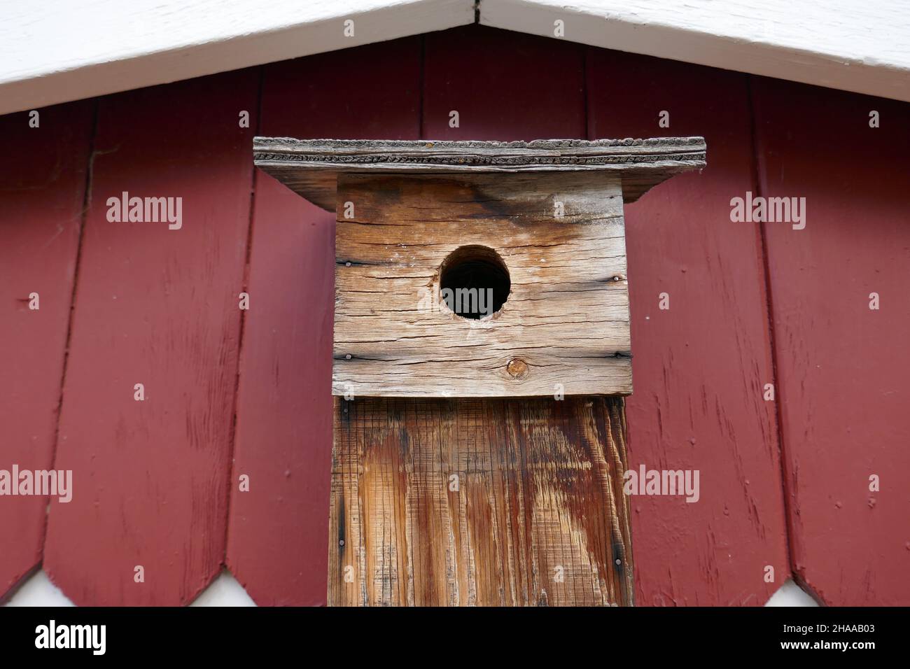 Old weathered wooden birdhouse on side of reed wooden house Stock Photo