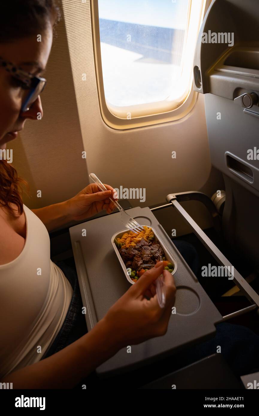 Caucasian woman flying in economy class and eating lunch from a tray ...