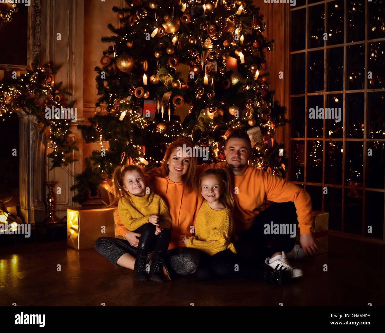 Happy family father mother and two small girls daughters in yellow sweaters sitting on floor together during Christmas Stock Photo