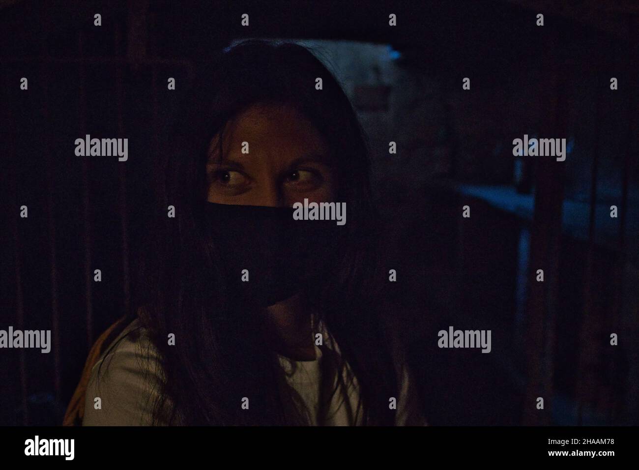 A closeup of a masked woman exploring a dark attic Stock Photo