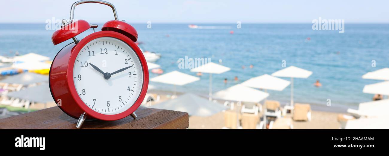 Red alarm clock standing on sea beach of hotel closeup Stock Photo