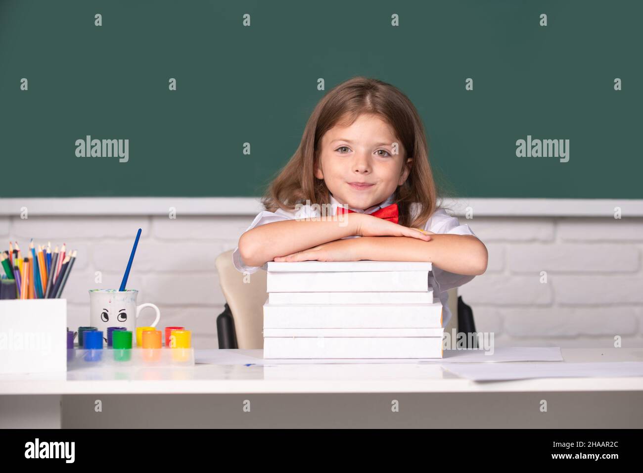 Smiling girl sitting at the desk and holding hands on the books in the ...