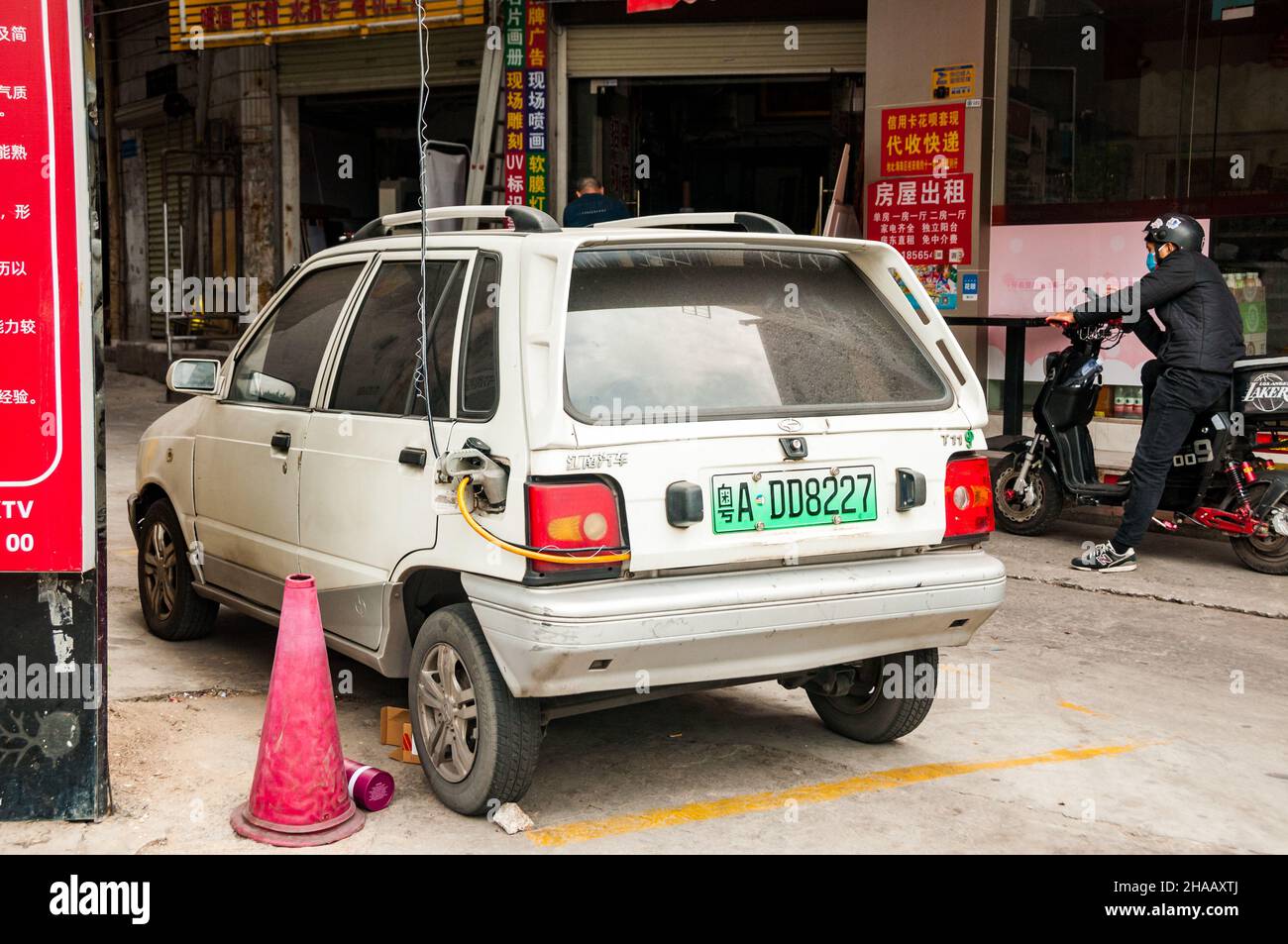 A Jiangnan T11, a Chinese made electrified version of the second generation Suzuki Alto, being charged by a jury rigged cable from a second floor wind Stock Photo