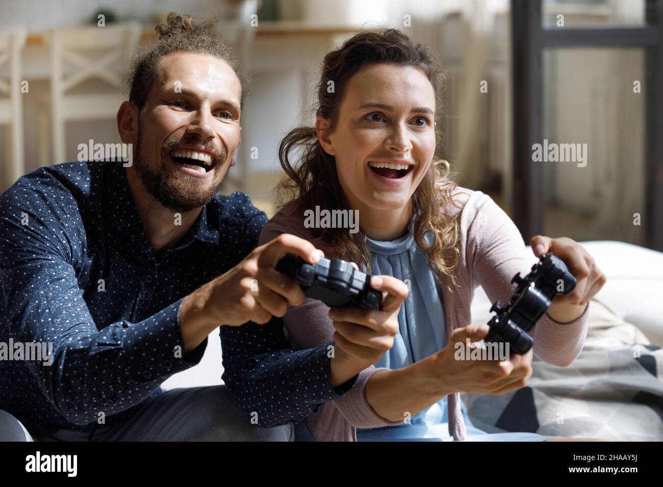 Happy joyful millennial couple enjoying virtual battle Stock Photo