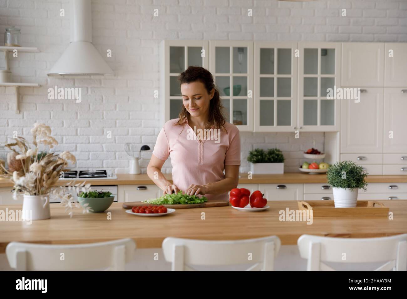 Happy homeowner woman cutting vegetables for salad in home kitchen Stock Photo
