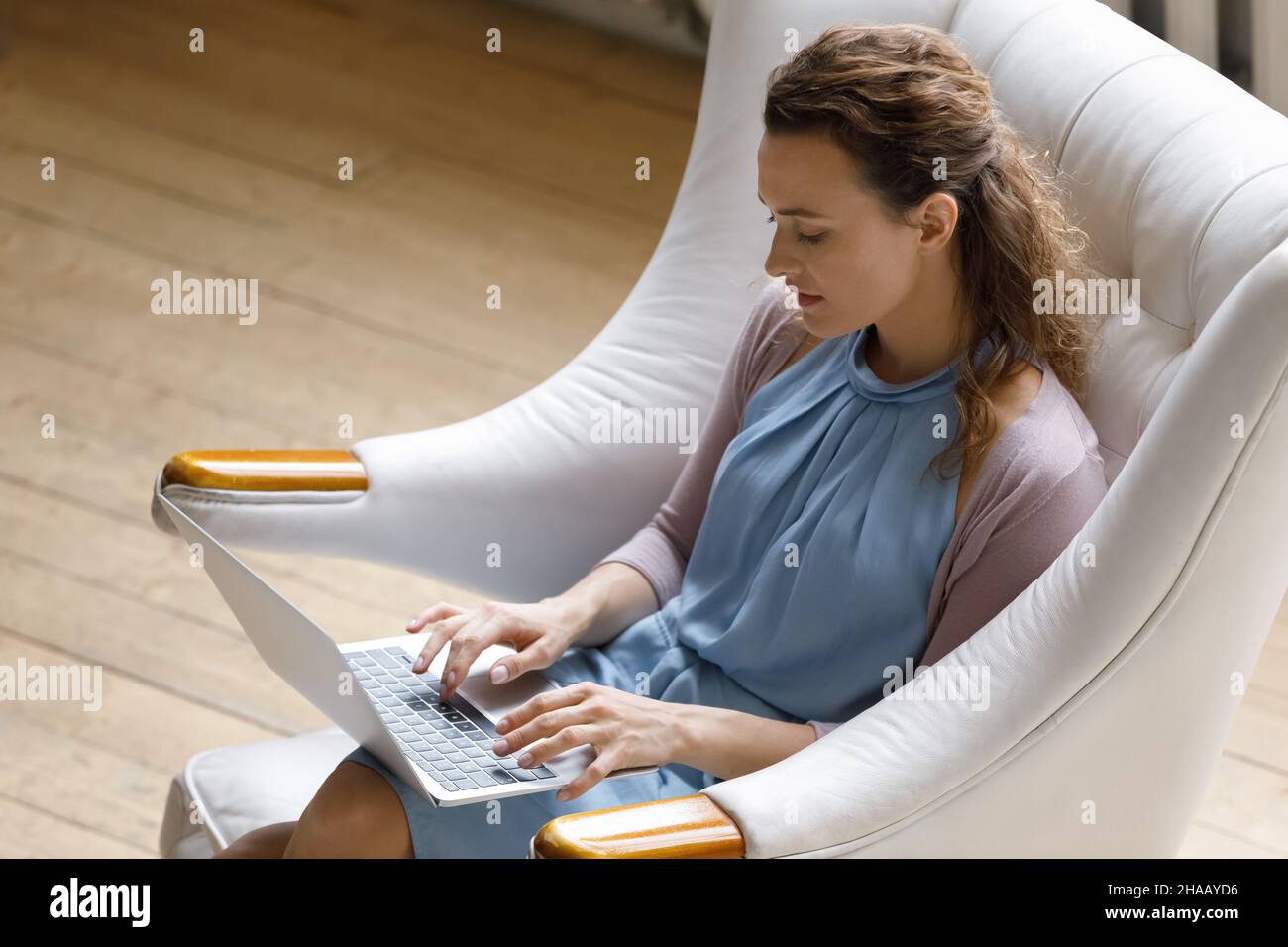 Focused young woman typing on laptop, resting in comfortable armchair Stock Photo